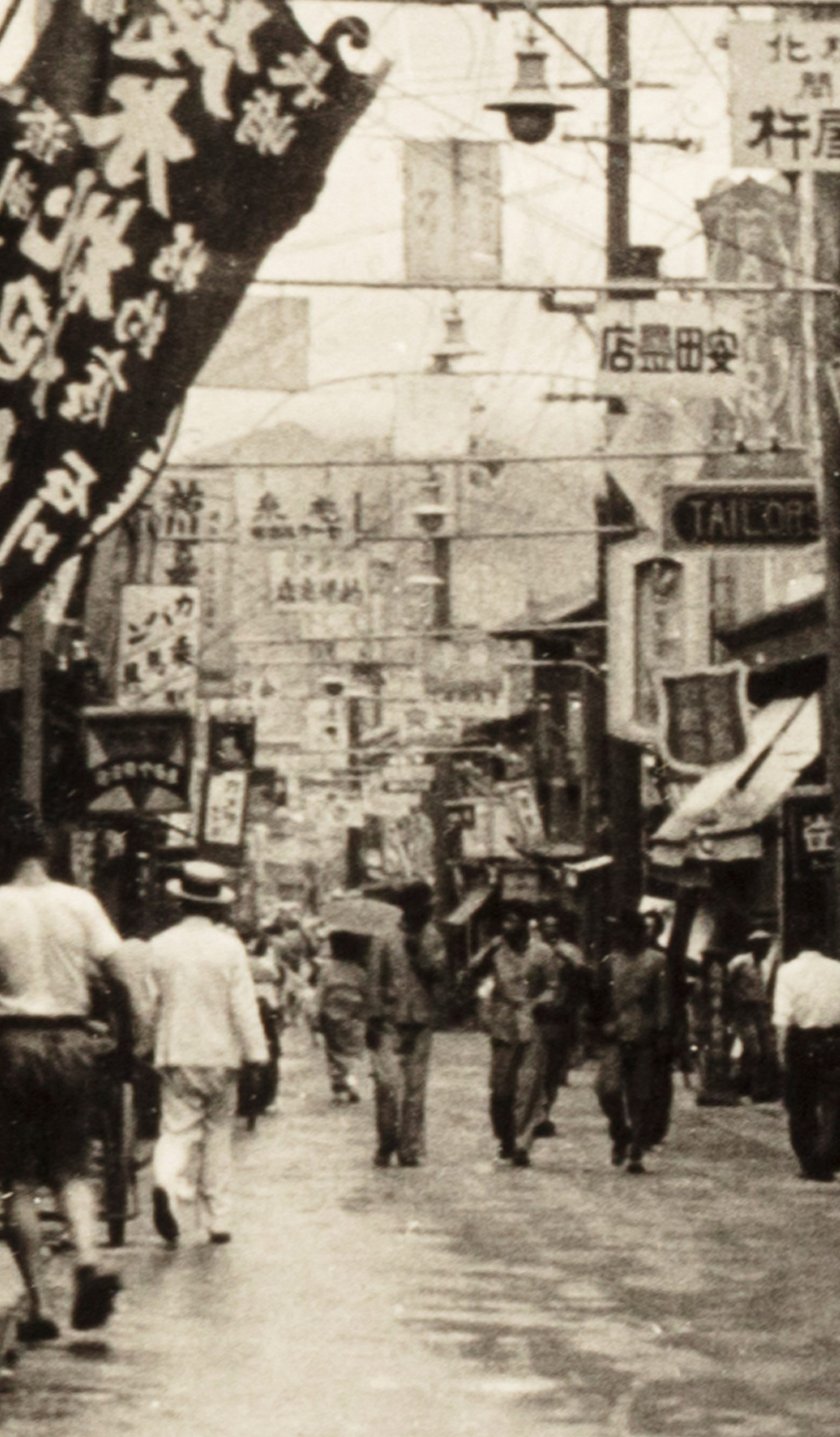 Black and white photograph of a street scene in Keijo, Korea, showing pedestrians walking either side along a banner filled street.