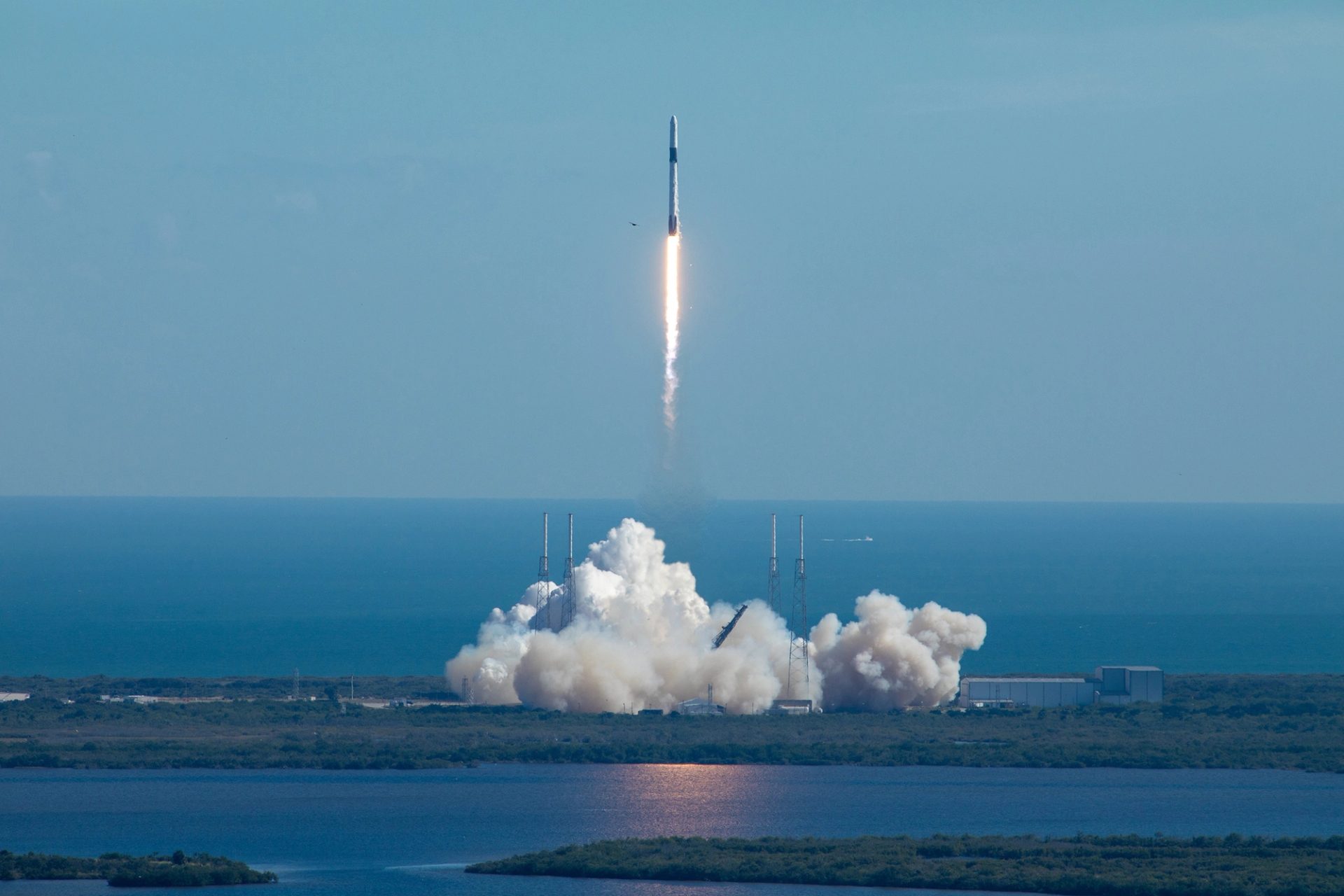A tall rocket with a long trail of burning fuel lifts off from a launchpad at Cape Canaveral.
