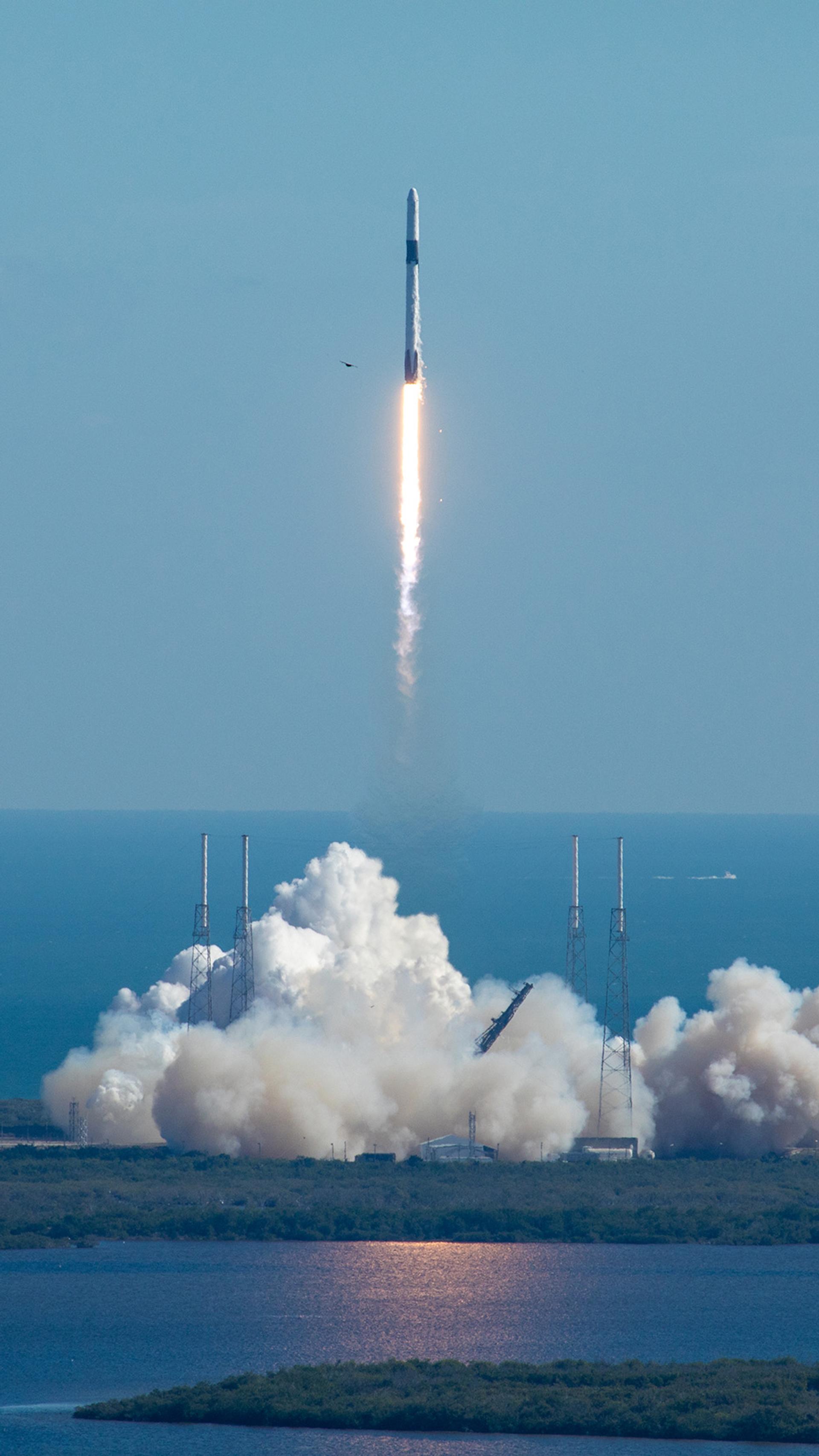 A tall rocket with a long trail of burning fuel lifts off from a launchpad at Cape Canaveral.