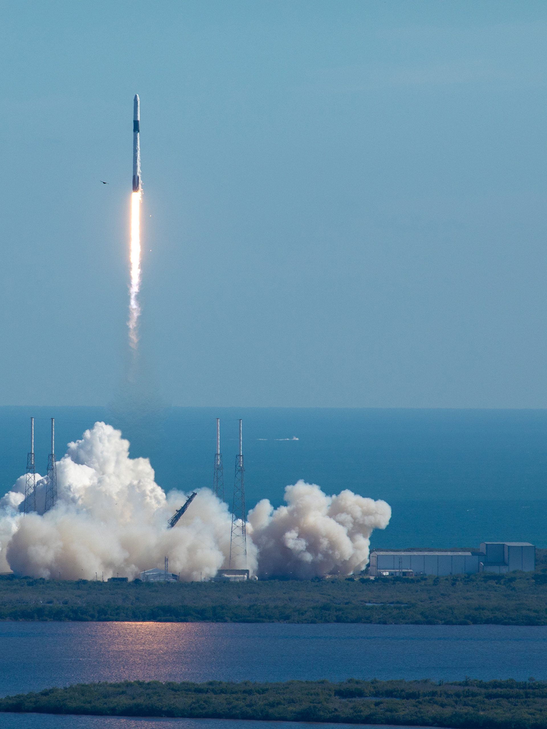 A tall rocket with a long trail of burning fuel lifts off from a launchpad at Cape Canaveral.