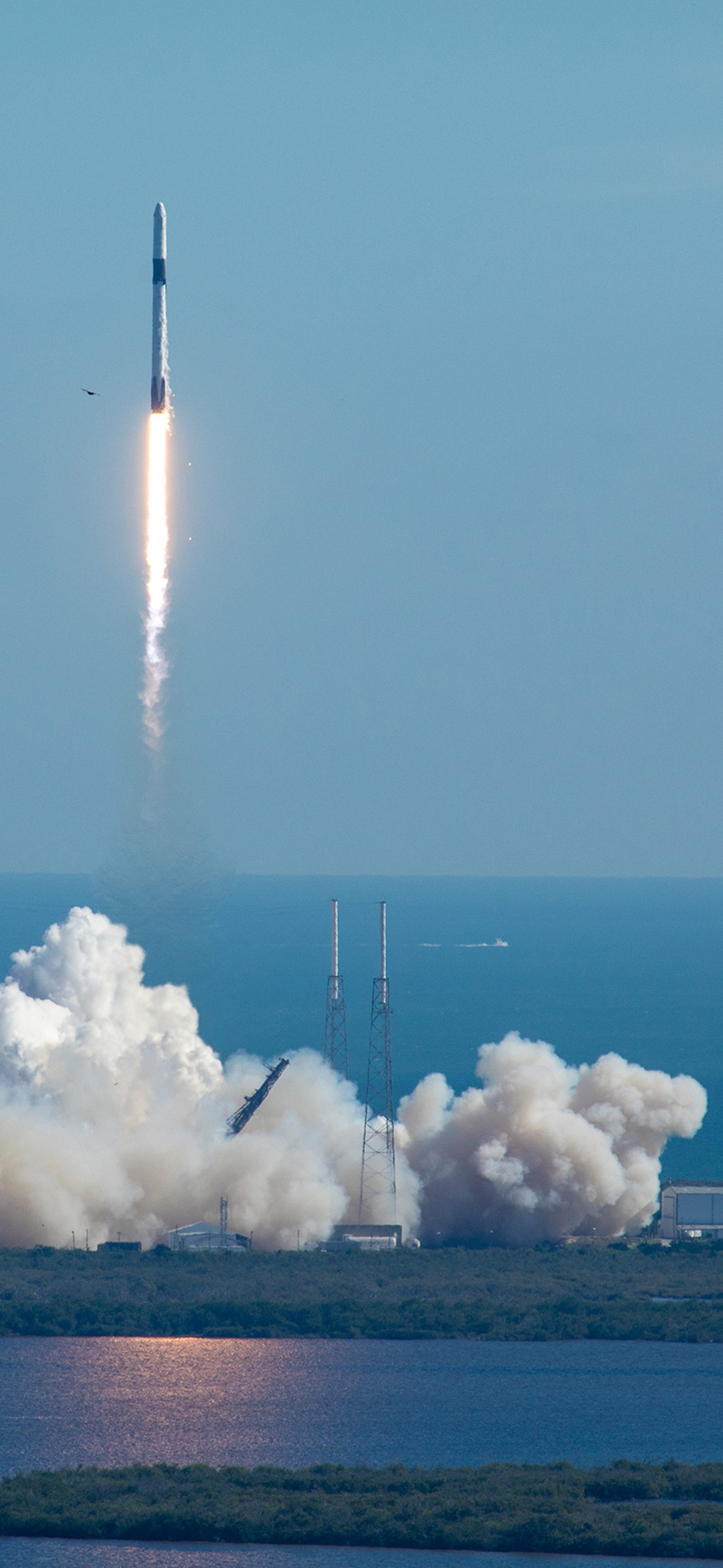 A tall rocket with a long trail of burning fuel lifts off from a launchpad at Cape Canaveral.