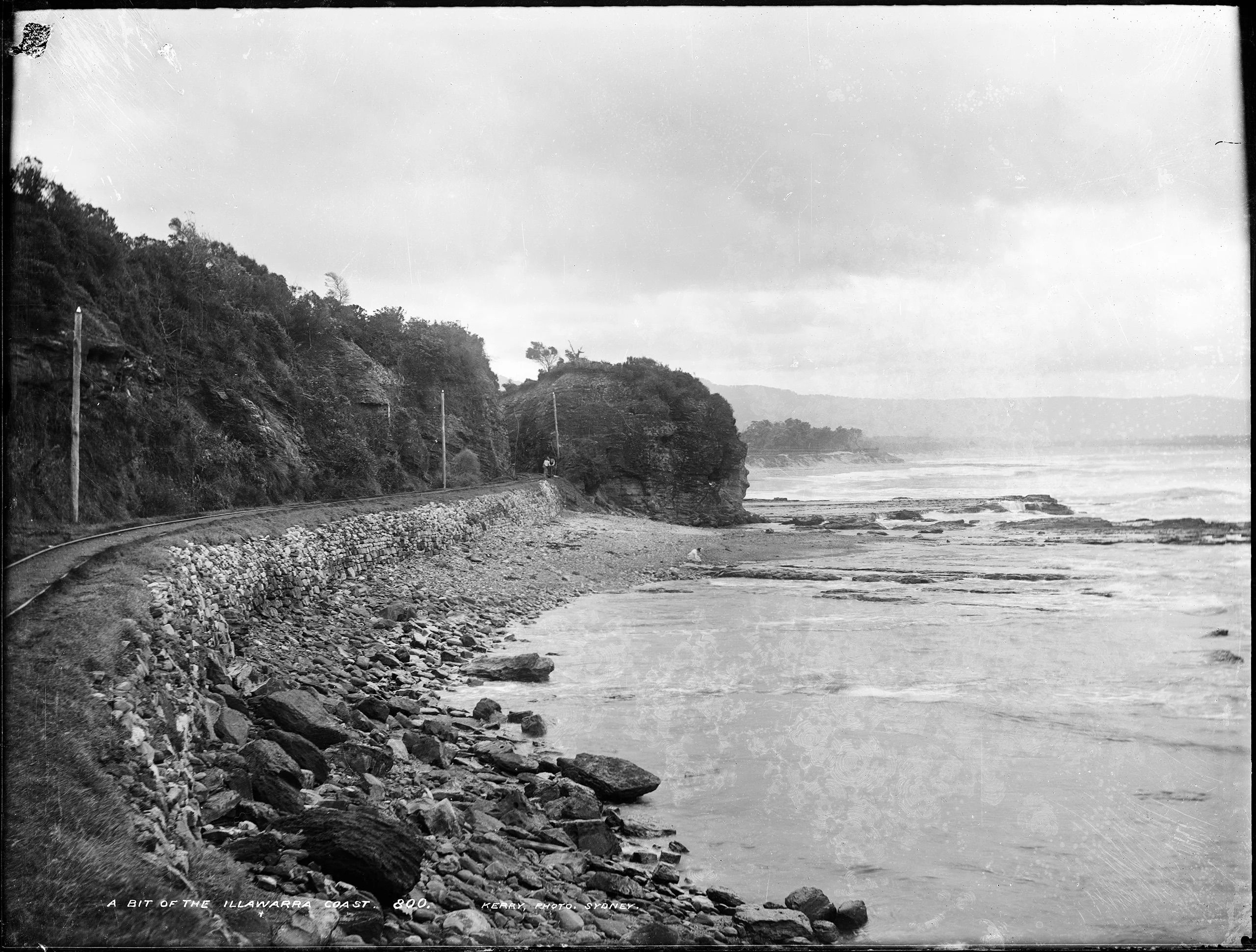 A railway track on a coastline. There are two men standing in the background.