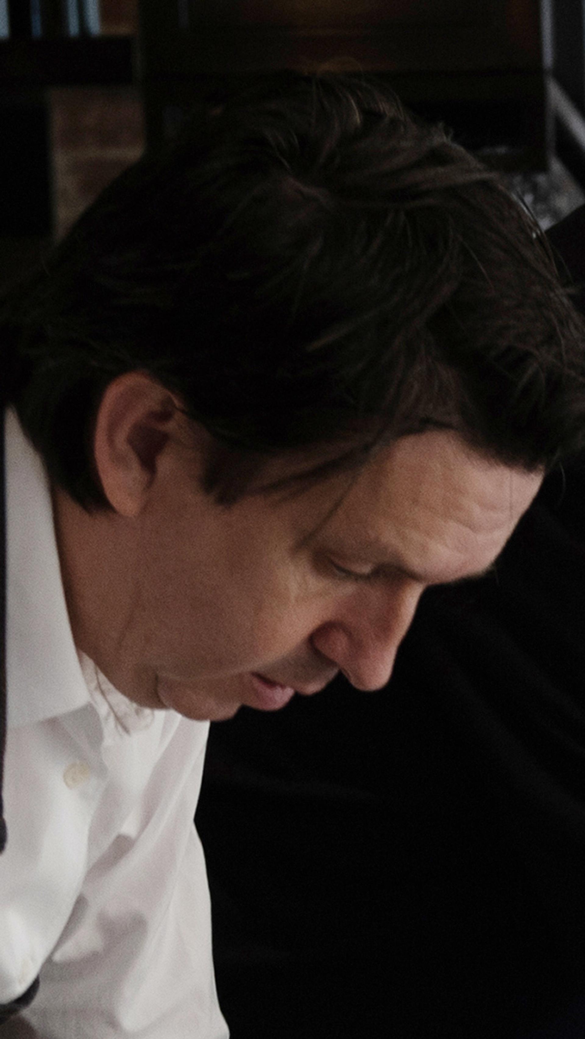 Two men looks down and over a table, in front of a brick wall.