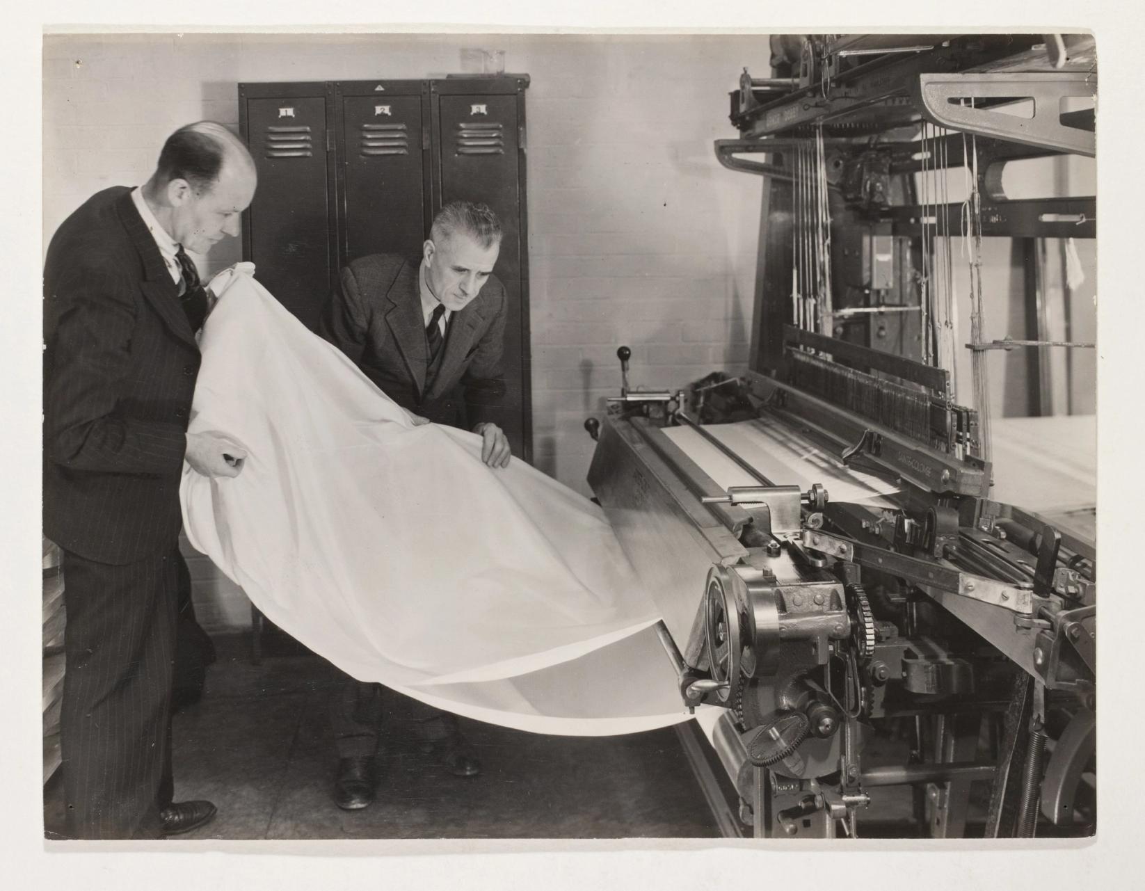 Black and white photograph depicting two men in suits examining a white fabric ('Terylene' synthetic material) being woven on an experimental loom.