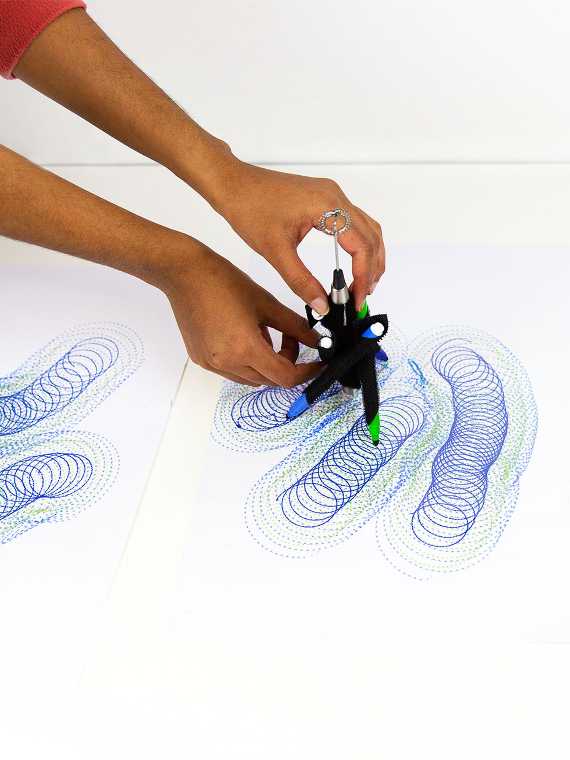 A series of spirograph drawings in blue and purple with hands controlling a DrawBot device.