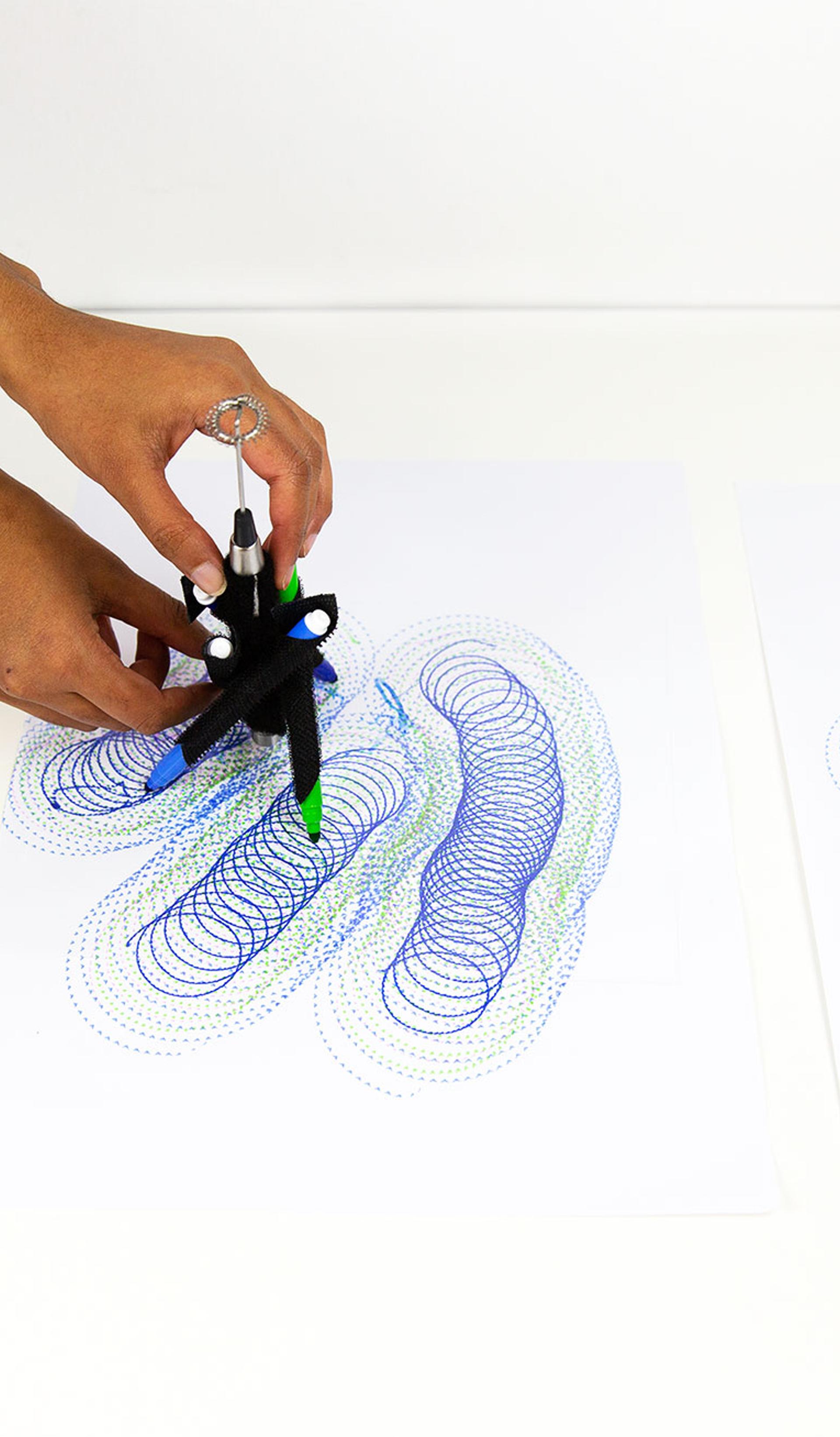 A series of spirograph drawings in blue and purple with hands controlling a DrawBot device.