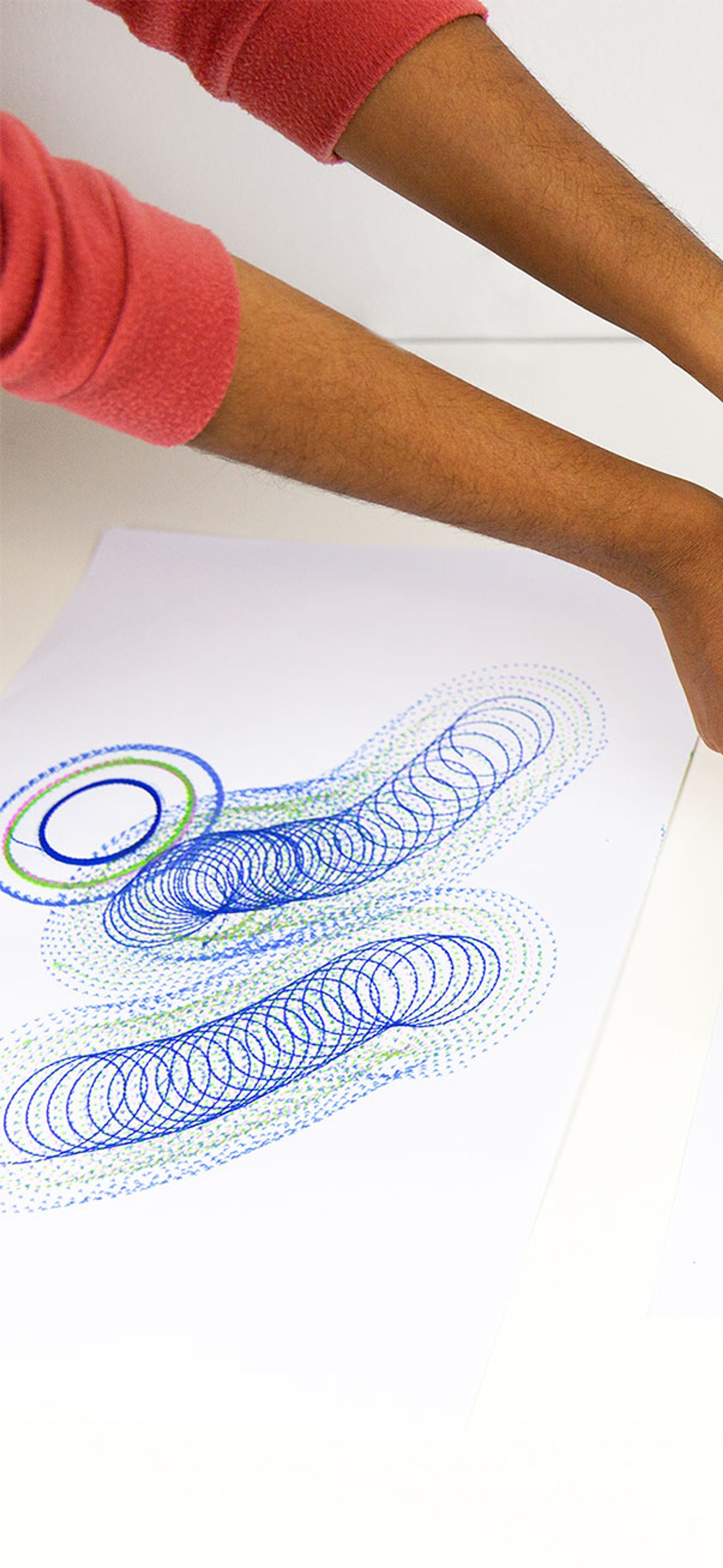 A series of spirograph drawings in blue and purple with hands controlling a DrawBot device.