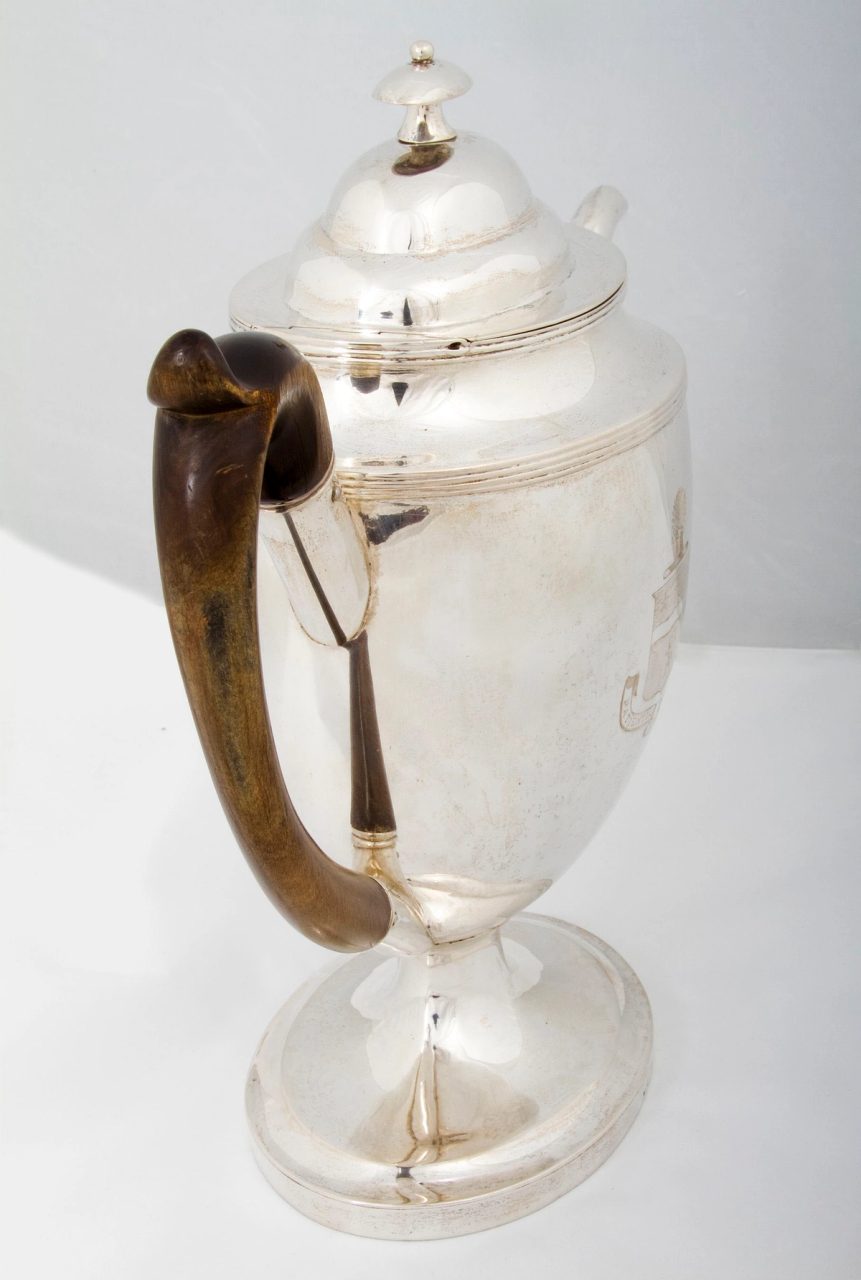A coffee pot with lid, made of silver and wood, with a c-shaped wooden handle.