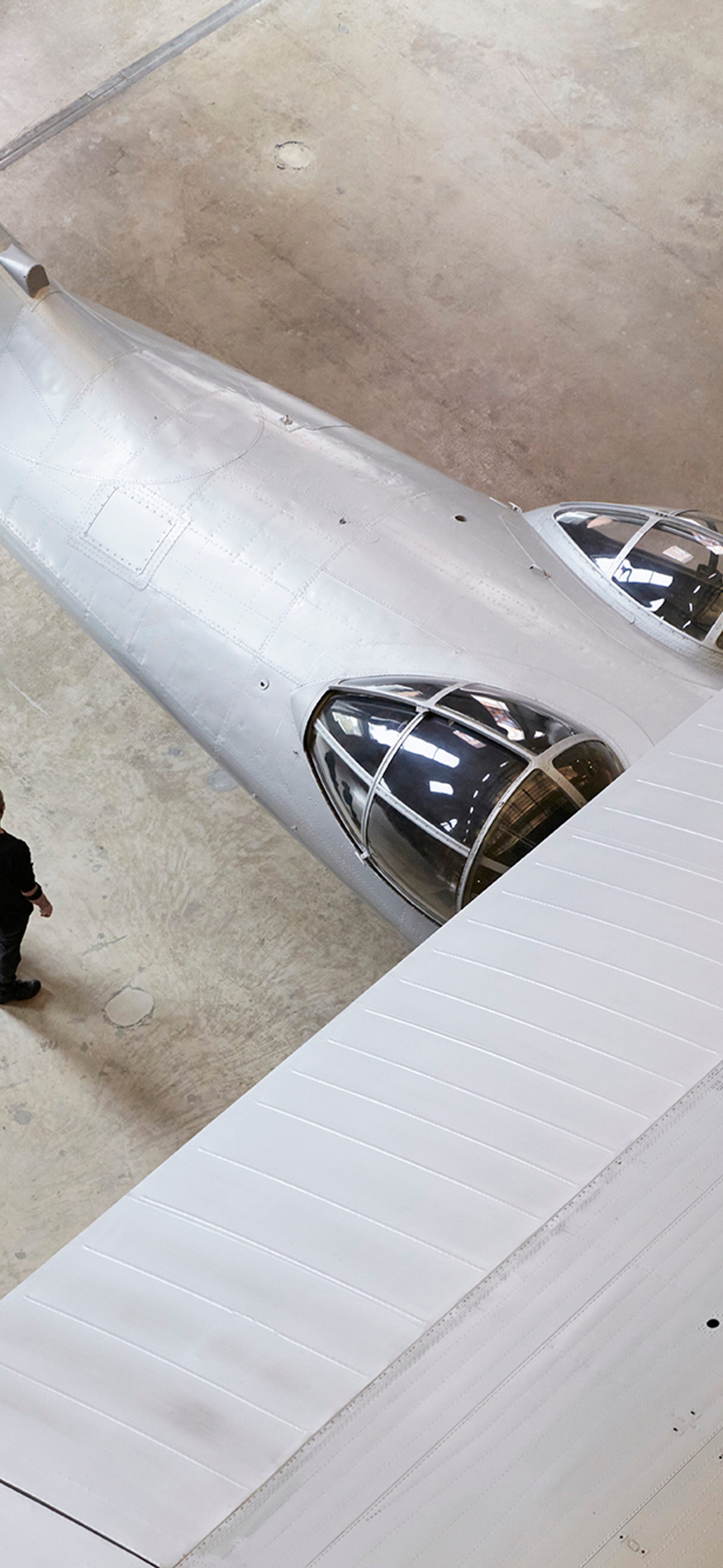 Partial aerial view of silver plane. Two people are standing close to the underneath of the wing.