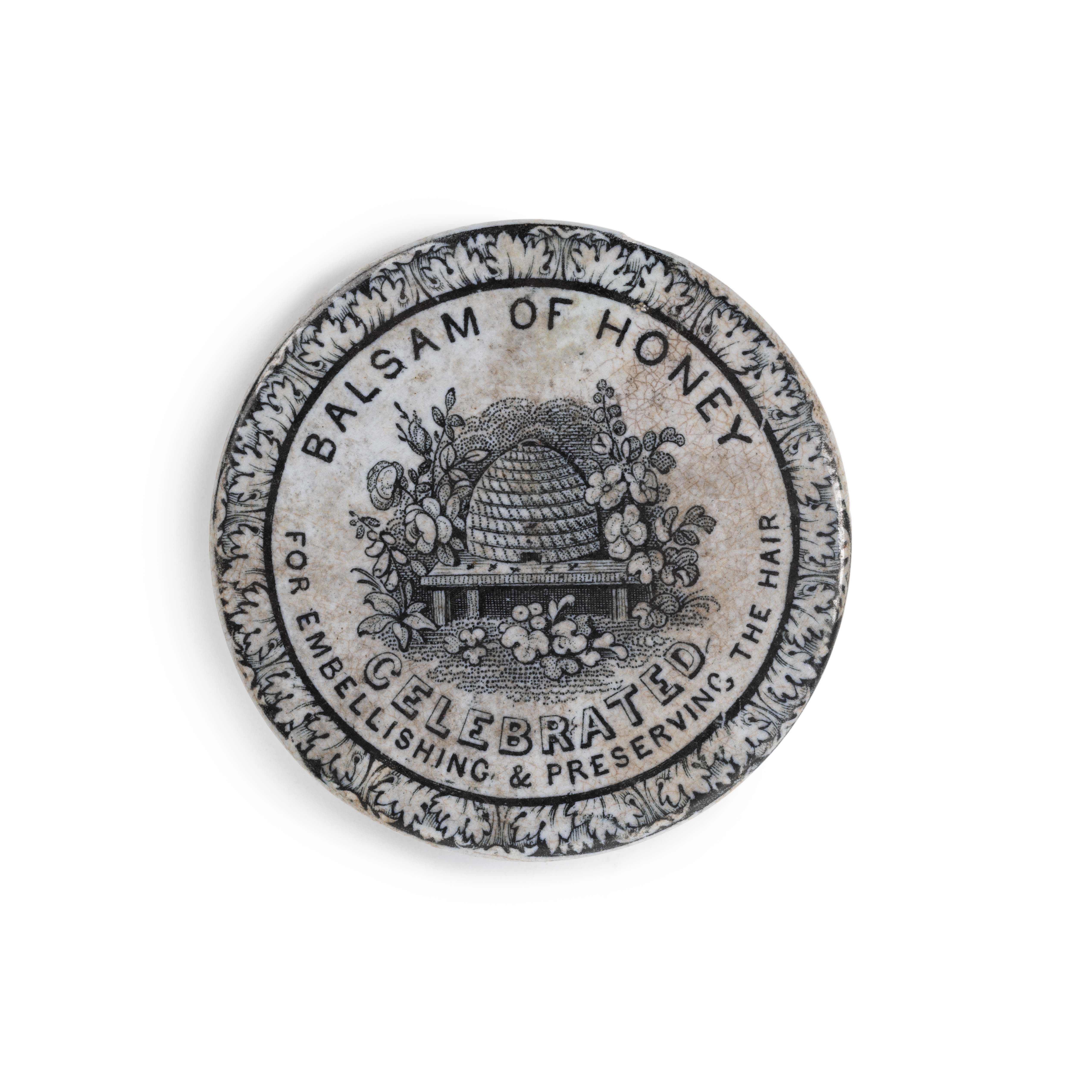 Ceramic lid of ‘Basalm of Honey’. Design includes floral border and in the centre, a beehive surrounded by flowers and plants.