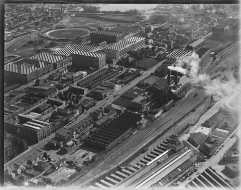 Black and white aerial photograph of the Ultimo Power House with smoke billowing out of its chimneys, and train lines to the bottom right corner