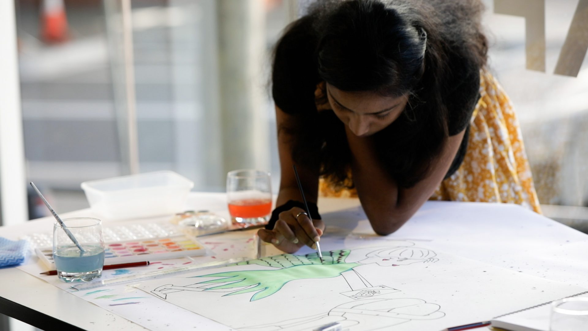 A Creative Studio student leans over a table and is painting