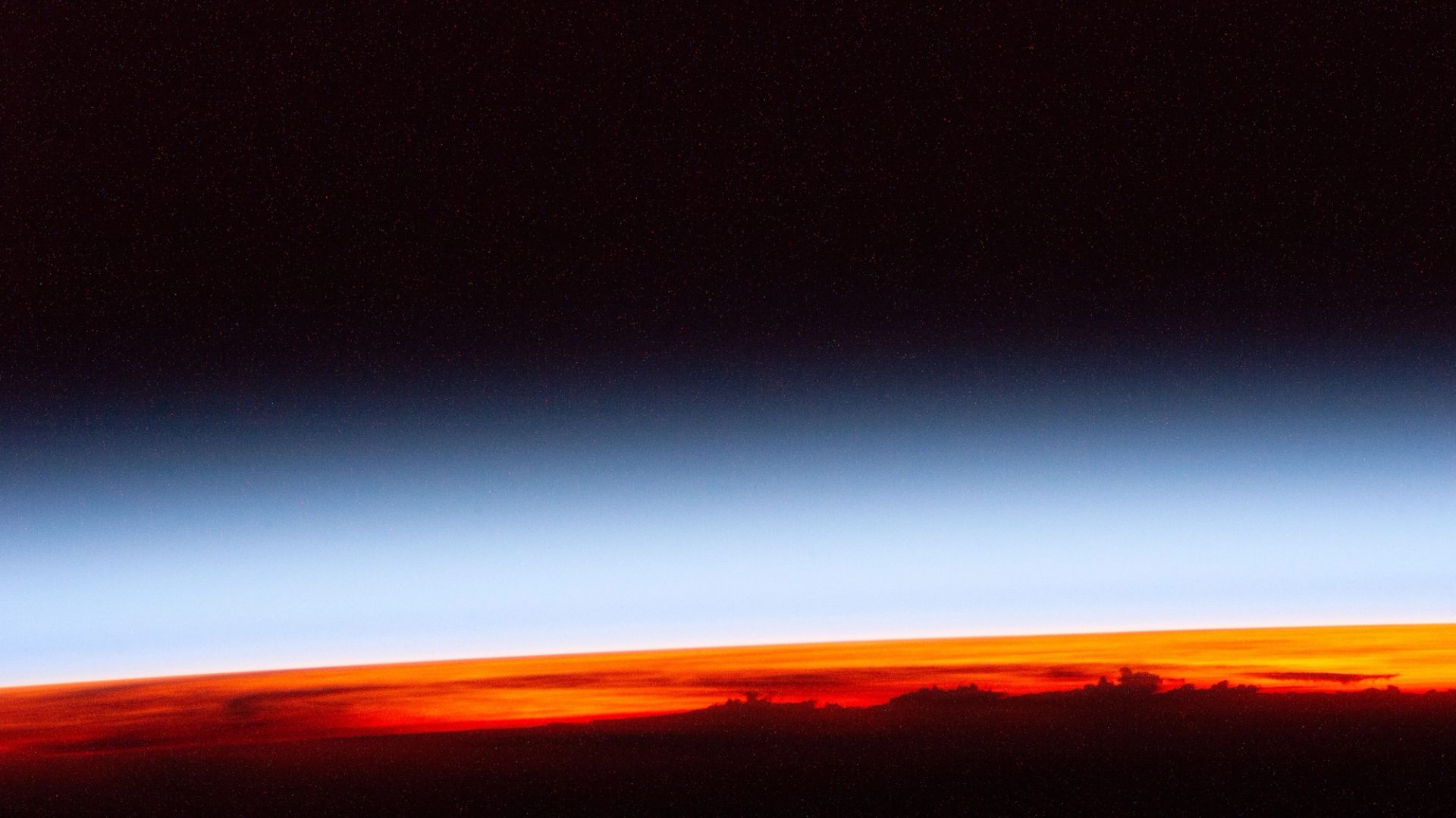 First rays of an orbital sunrise from the International Space Station, with a black, blue and bright orange gradient of the sunrise.