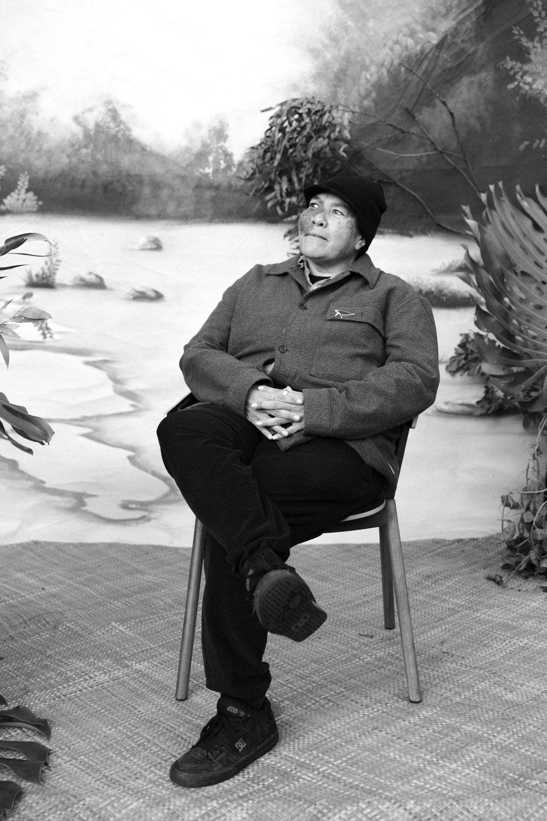 A Gumbaynggirr woman sits on a chair in front of a painted backdrop.