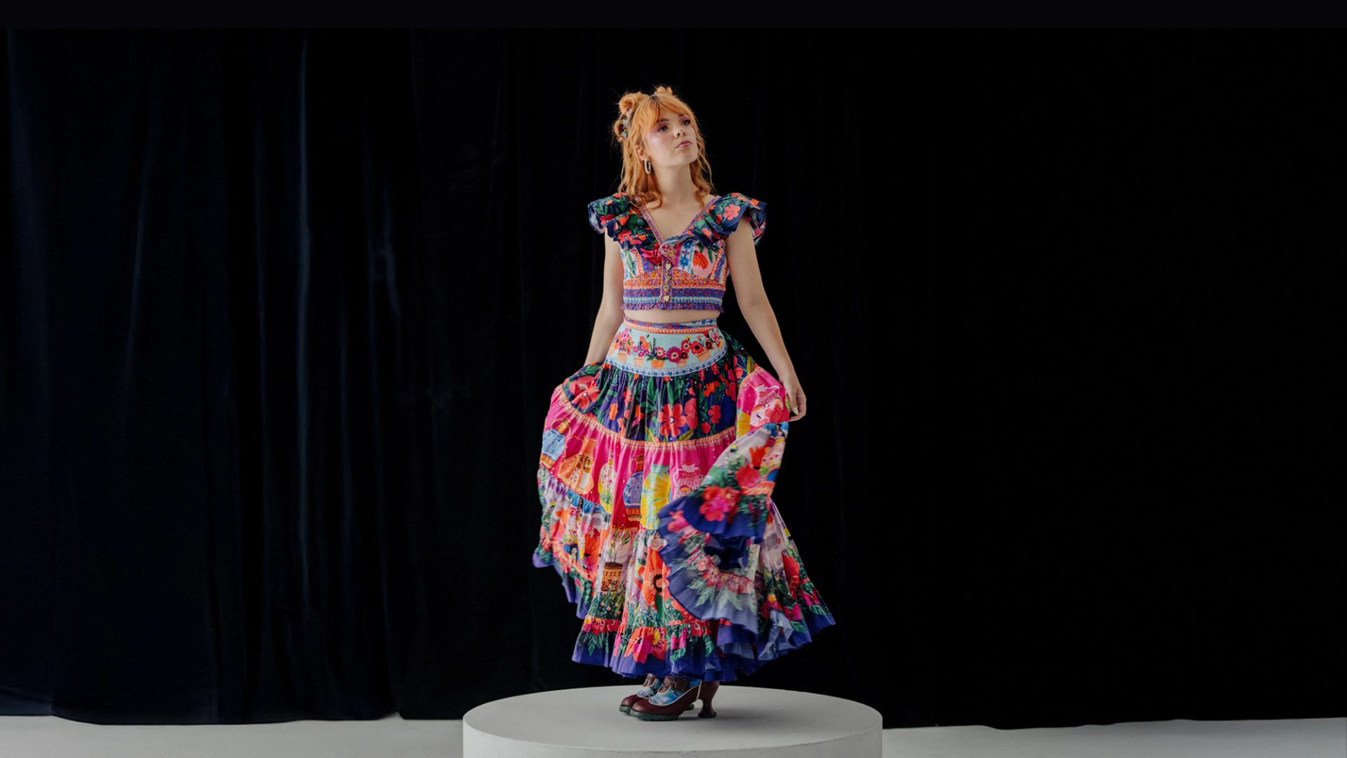 Activist Chloe Hayden posed in the centre, wearing a vibrant, multi-patterned dress against a black background.