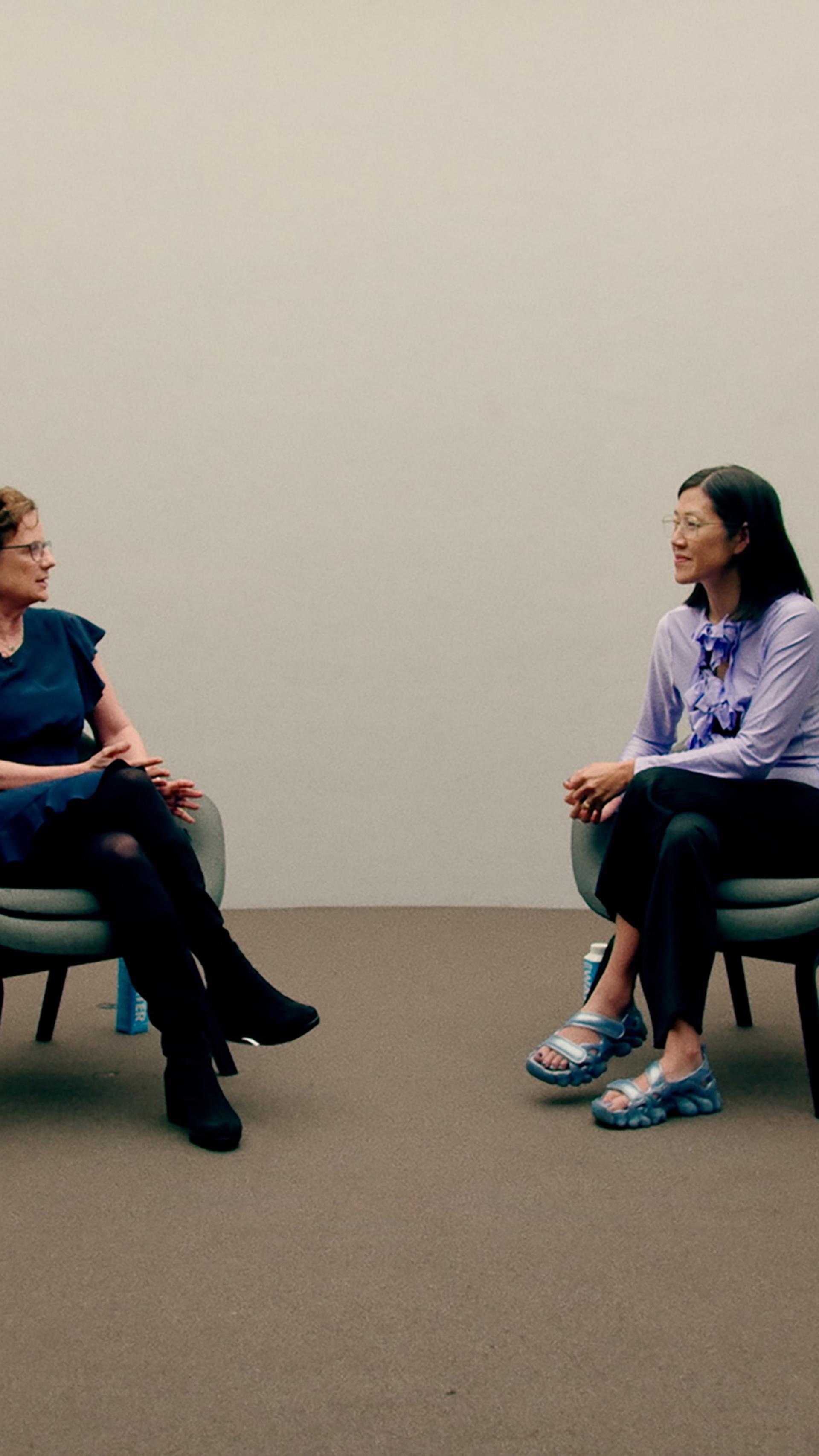 Two women sit in chairs conversing.