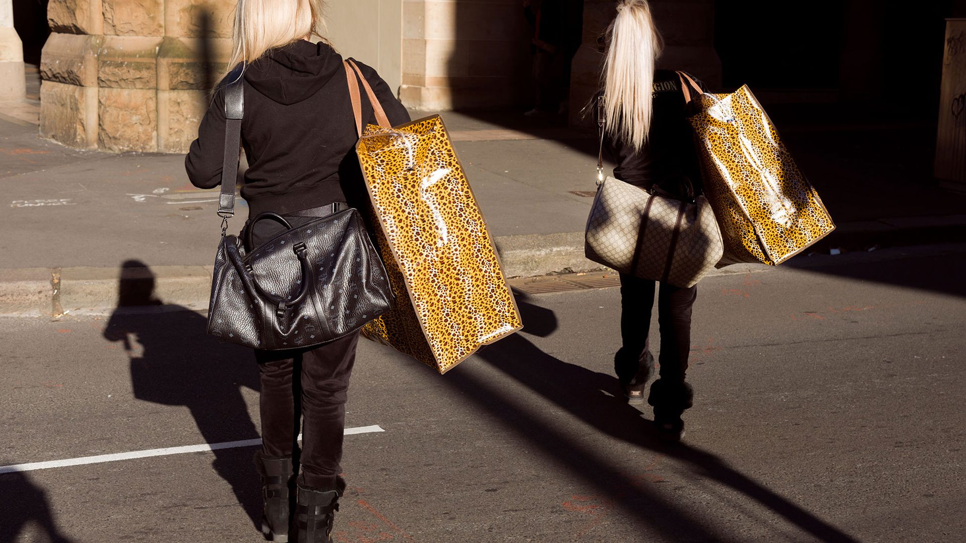 Two figures with blonde hair walk through the Haymarket carrying leopard print bags.