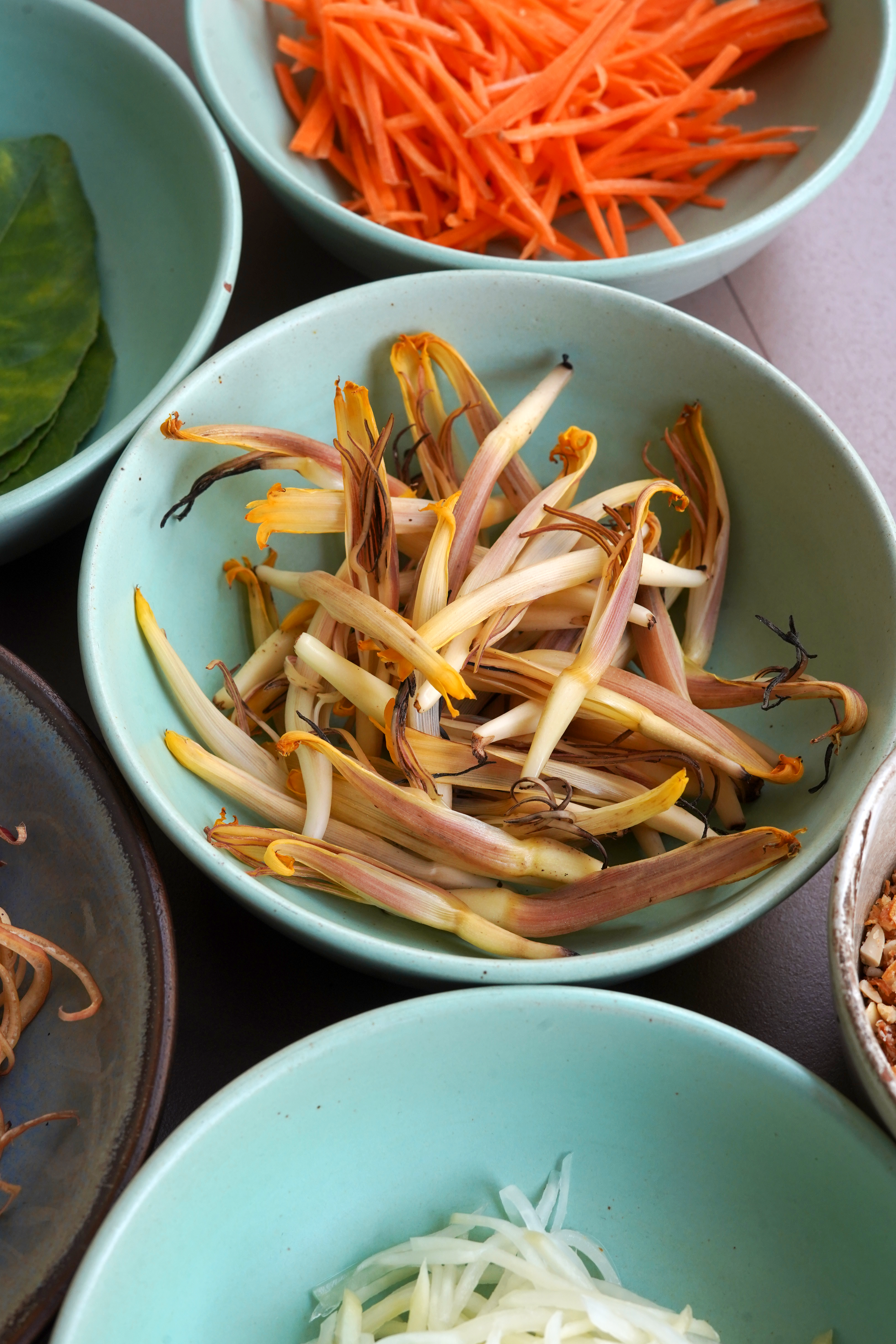 A small blue bowl with cleaned and chopped mocha flowers. Above, the same style bowl filled with finely chopped fresh carrot.