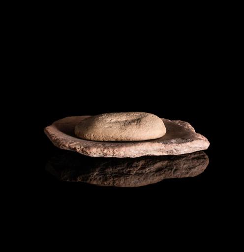A beige stone grindstone and mill against a deep black background