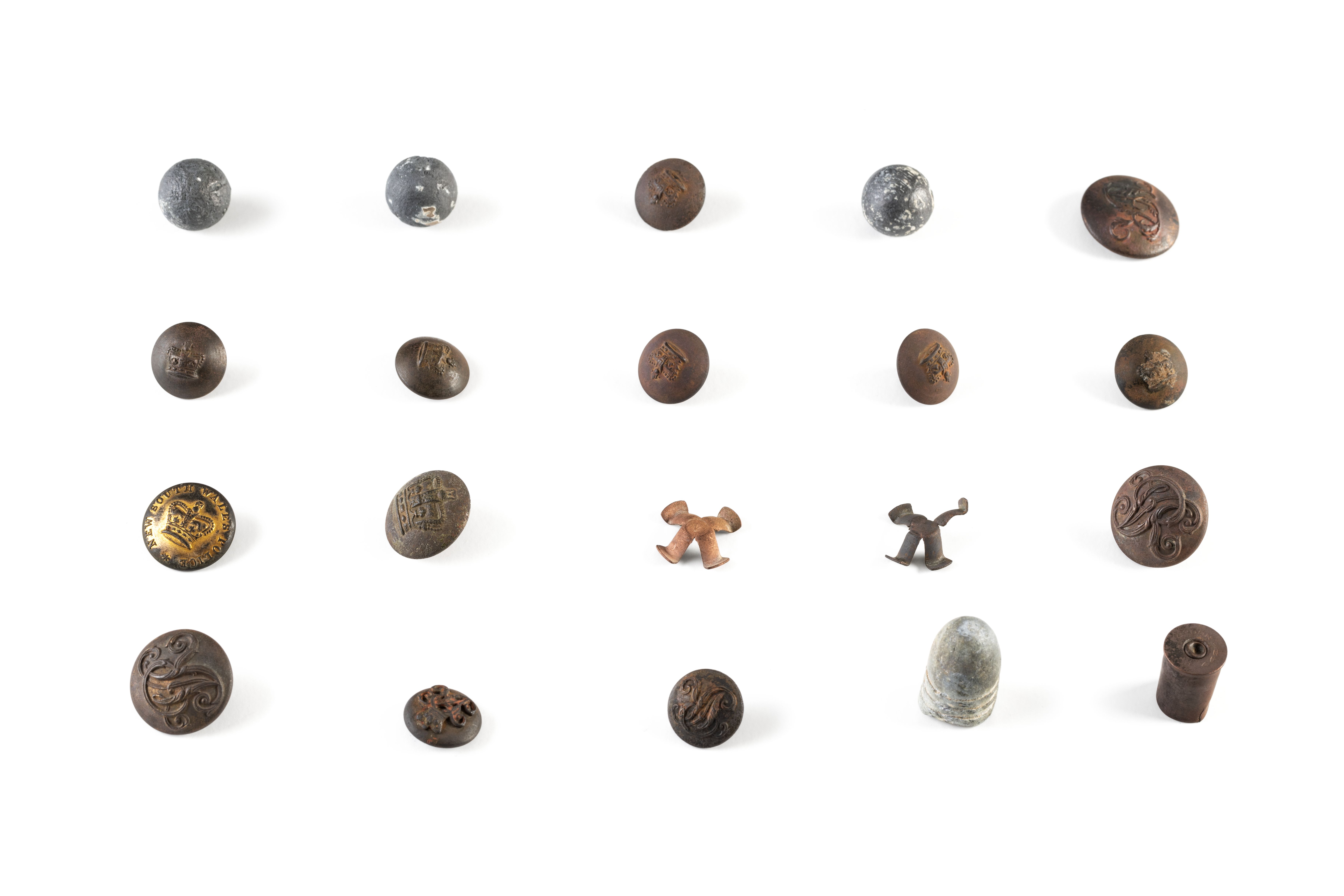 Collection of buttons and ammunition used by the Native Police. The thirteen circular metal buttons vary in size and design, however all referring to the reign of Queen Victoria, either depicting a crown or the initials VR or both, in raised embossed designs. Ammunition includes three spherical lead carbine balls and two brass percussion caps from a Potts & Hunt double barrelled carbine, a bullet cartridge from a .577 Snider-Enfield carbine and a brass cartridge casing for a .442 cartridge used in a Webley centre fire revolver.