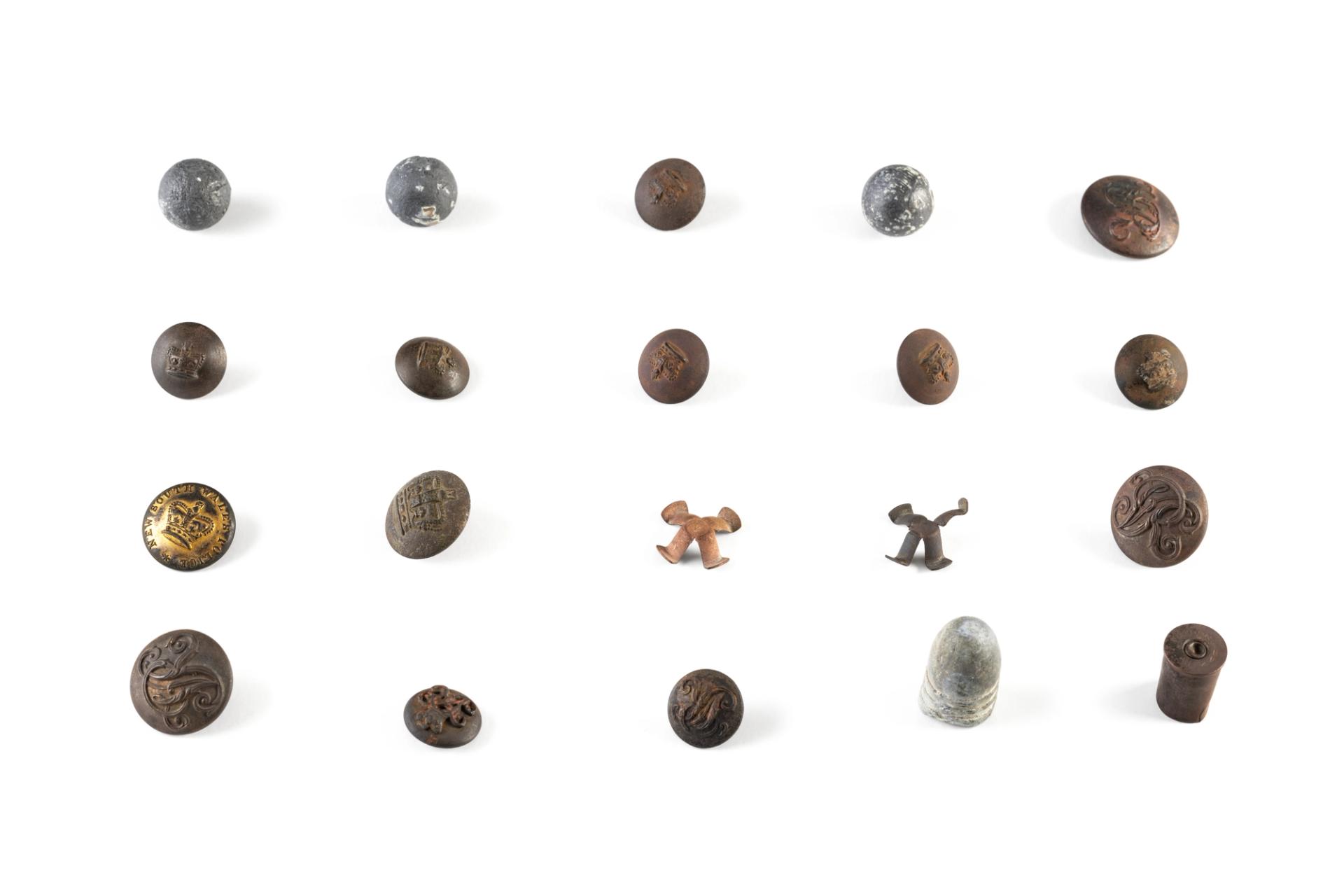 Collection of buttons and ammunition used by the Native Police. The thirteen circular metal buttons vary in size and design, however all referring to the reign of Queen Victoria, either depicting a crown or the initials VR or both, in raised embossed designs. Ammunition includes three spherical lead carbine balls and two brass percussion caps from a Potts & Hunt double barrelled carbine, a bullet cartridge from a .577 Snider-Enfield carbine and a brass cartridge casing for a .442 cartridge used in a Webley centre fire revolver.