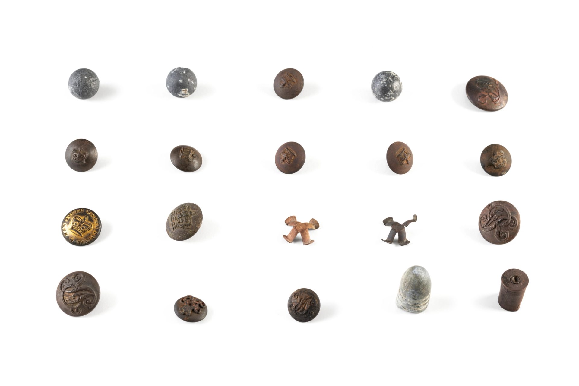 Collection of buttons and ammunition used by the Native Police. The thirteen circular metal buttons vary in size and design, however all referring to the reign of Queen Victoria, either depicting a crown or the initials VR or both, in raised embossed designs. Ammunition includes three spherical lead carbine balls and two brass percussion caps from a Potts & Hunt double barrelled carbine, a bullet cartridge from a .577 Snider-Enfield carbine and a brass cartridge casing for a .442 cartridge used in a Webley centre fire revolver.