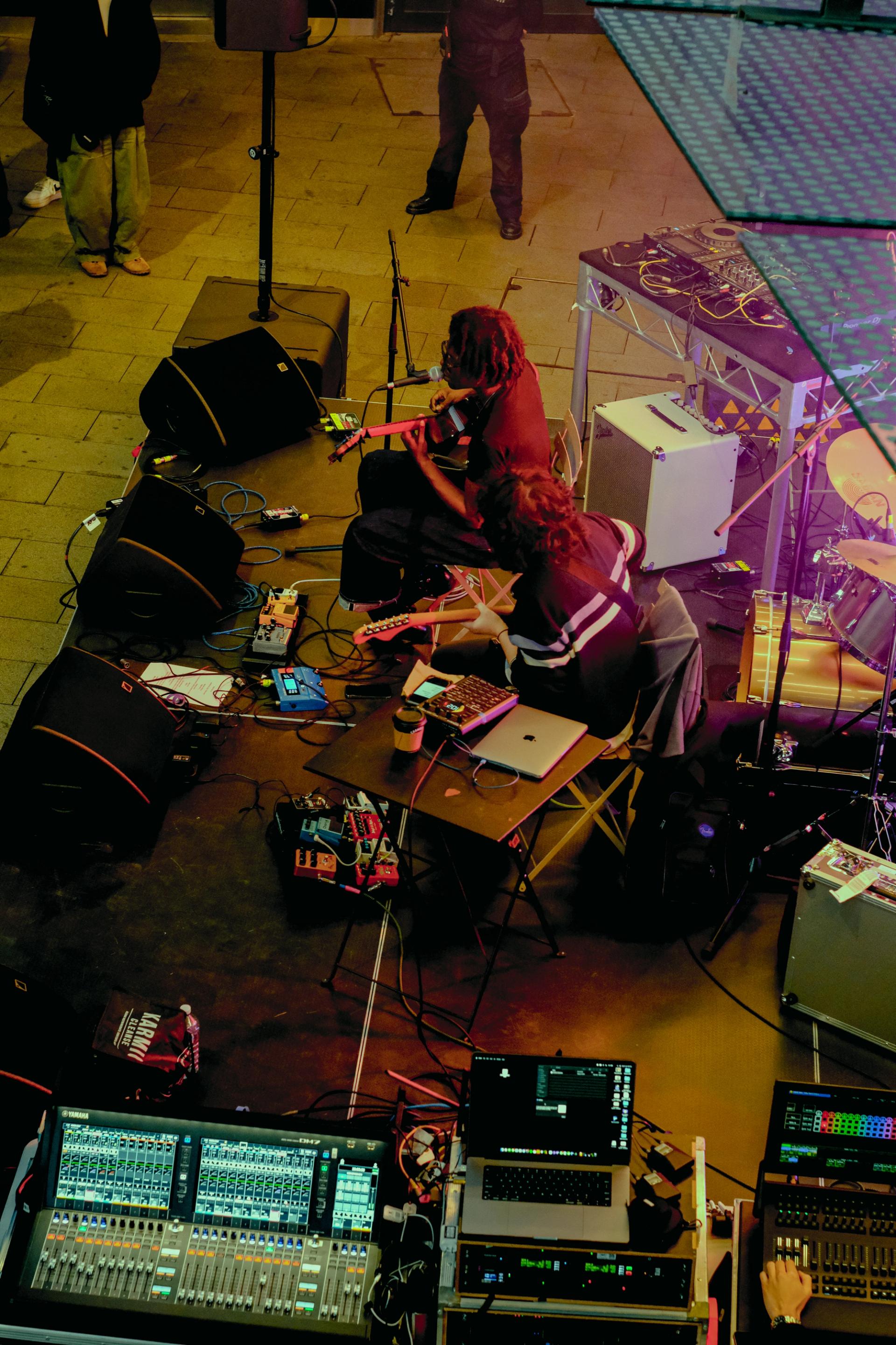 An overhead shot of the musician FRIDAY* performing a street show in Parramatta. He is depicted sitting on a chair, guitar in hand. A bandmate is next to him, also holding a guitar.