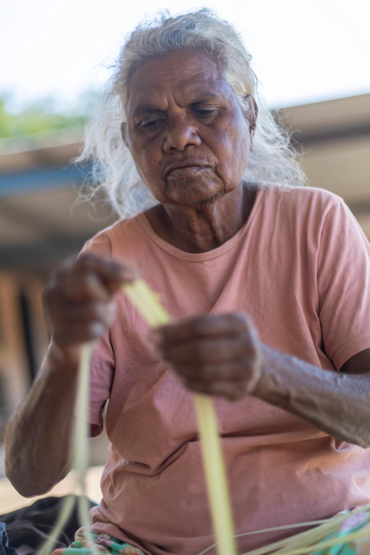 A woman sitting and holding a piece of pandanus in her hands.