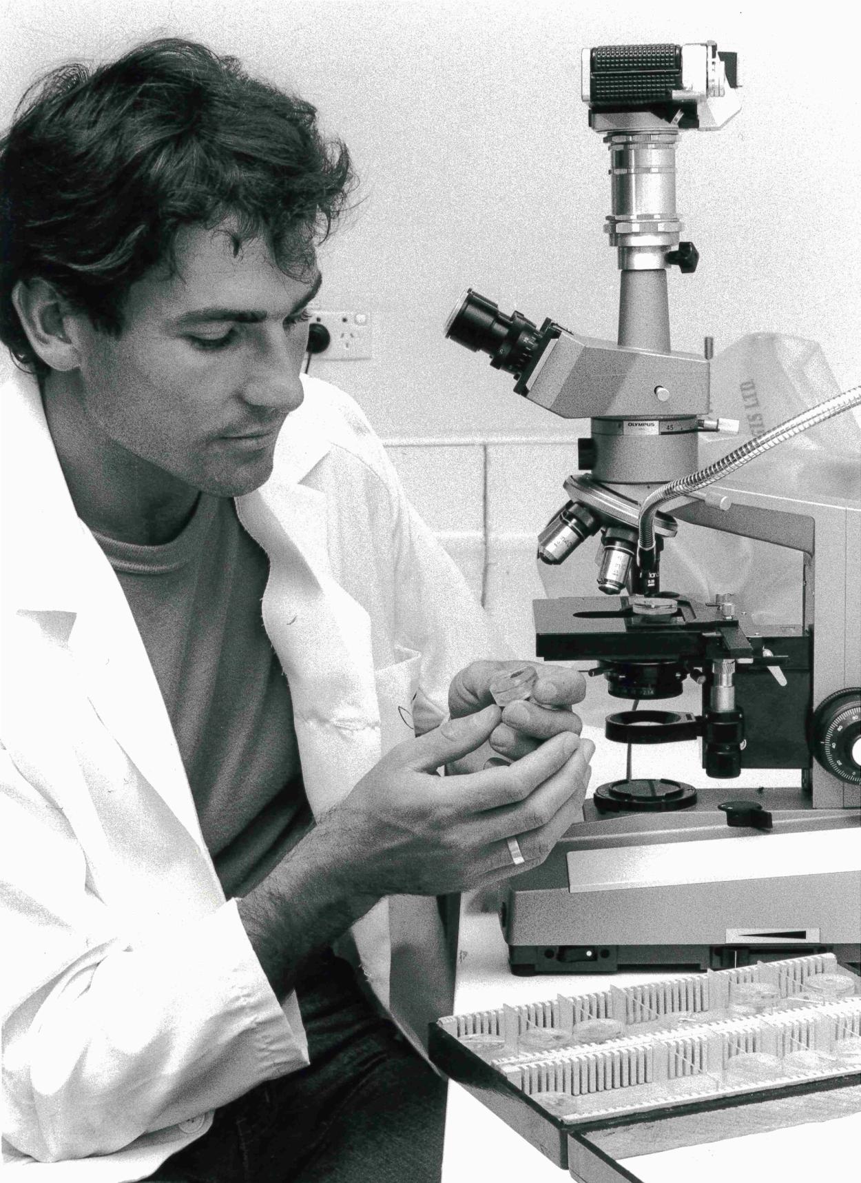 Black and white image of a museum employee working in a conservation lab with microscope