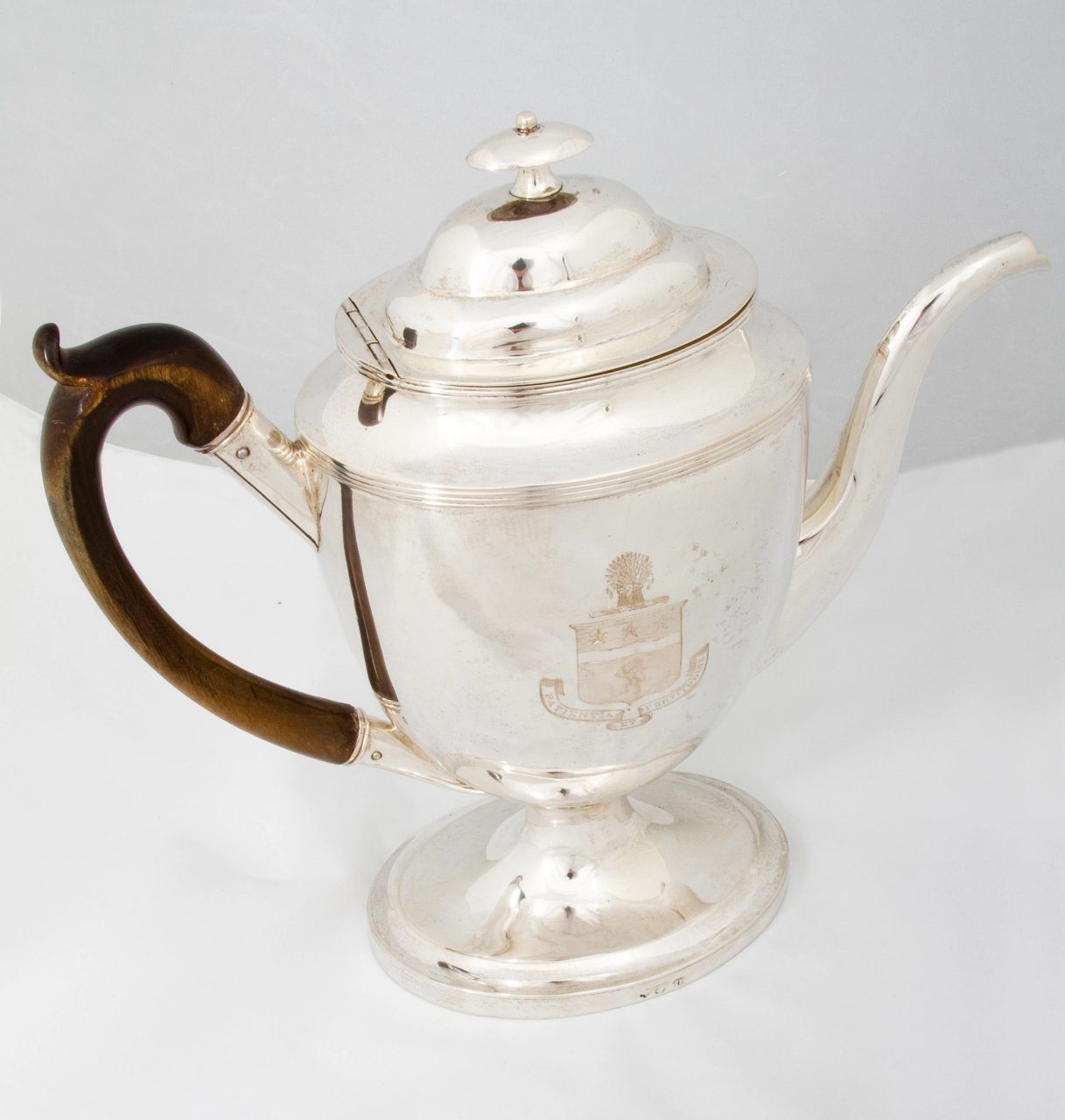 A coffee pot with lid, made of silver and wood, with a c-shaped wooden handle.