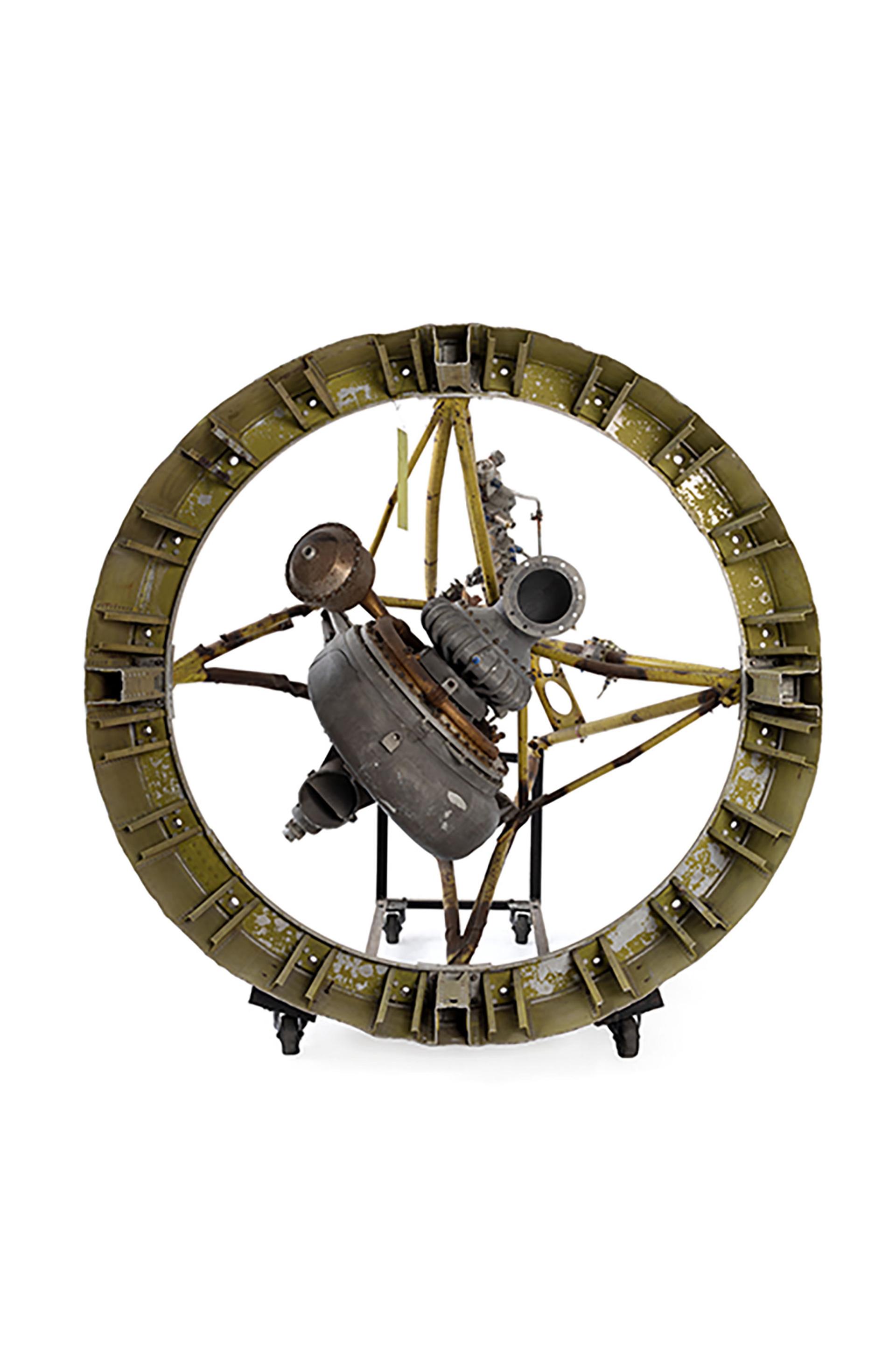 A rocket engine composed on a large metal circular frame with an engine secured from four points in the centre.