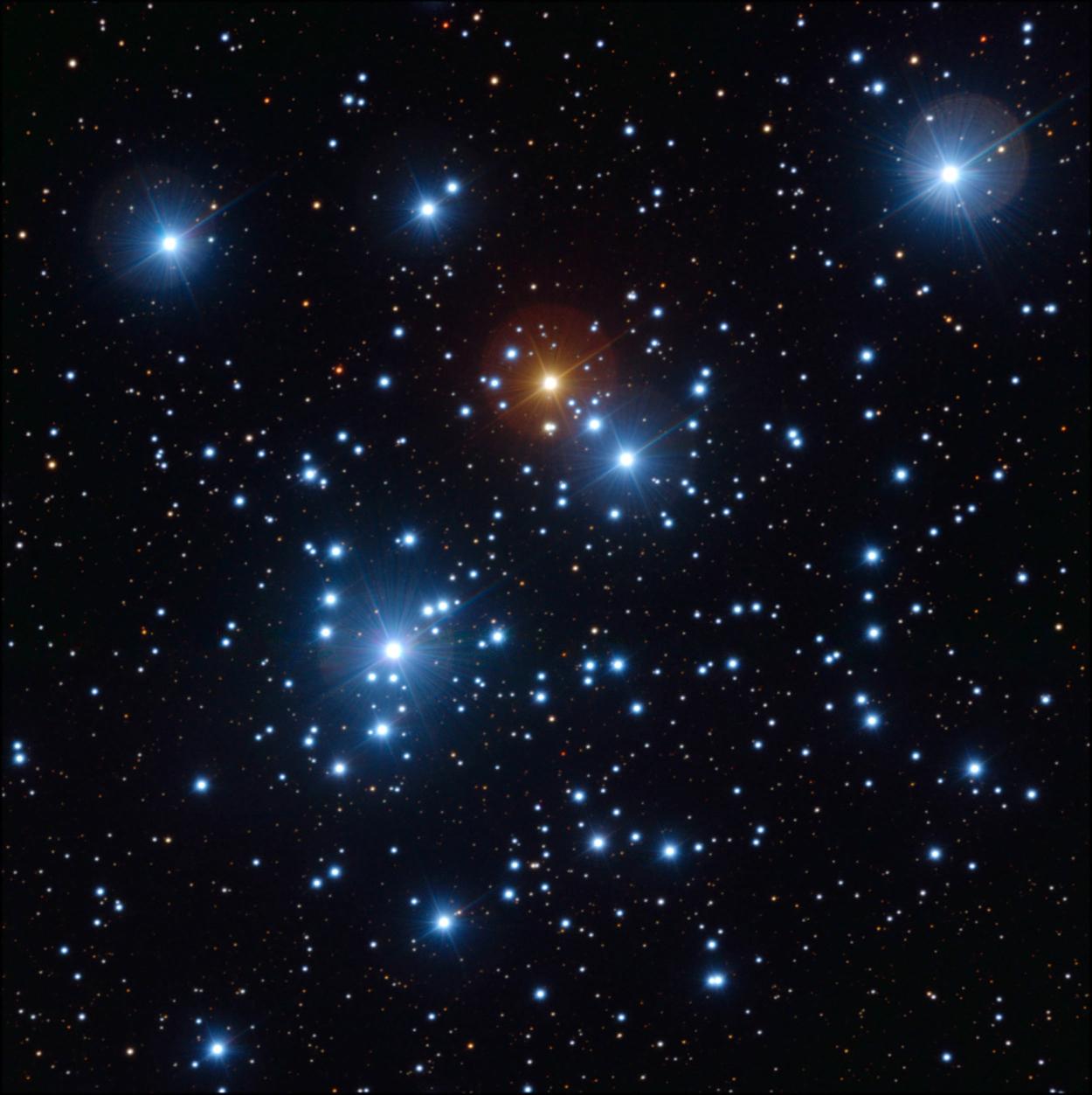 Colour image of a group of stars. There are several very bright blue stars, and one very bright red star.
