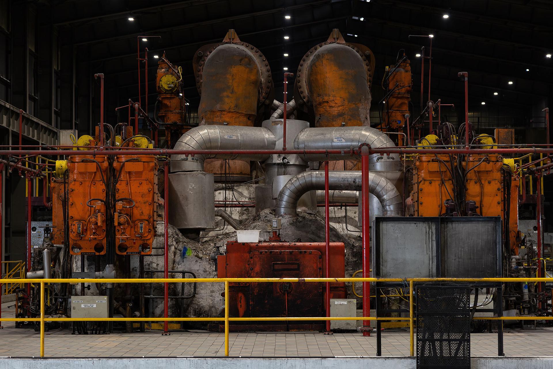 Mechanical and industrial equipment in colours of red, silver and orange sit behind a yellow safety fence.