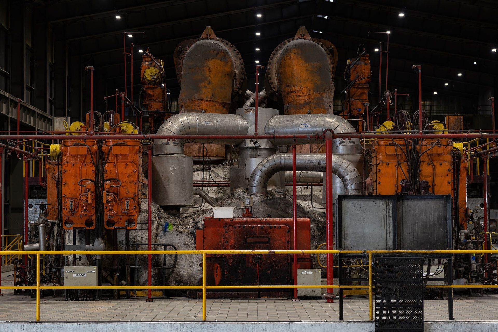Mechanical and industrial equipment in colours of red, silver and orange sit behind a yellow safety fence.