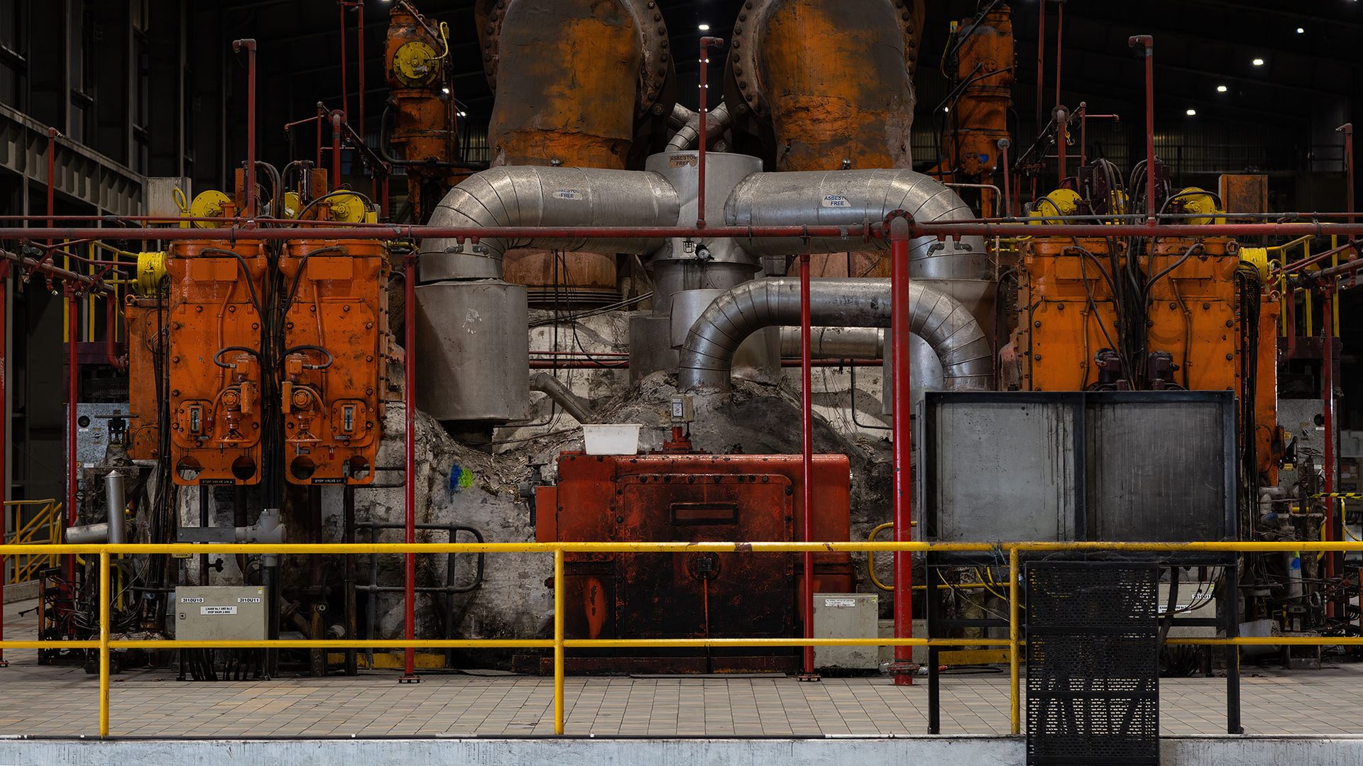 Mechanical and industrial equipment in colours of red, silver and orange sit behind a yellow safety fence.