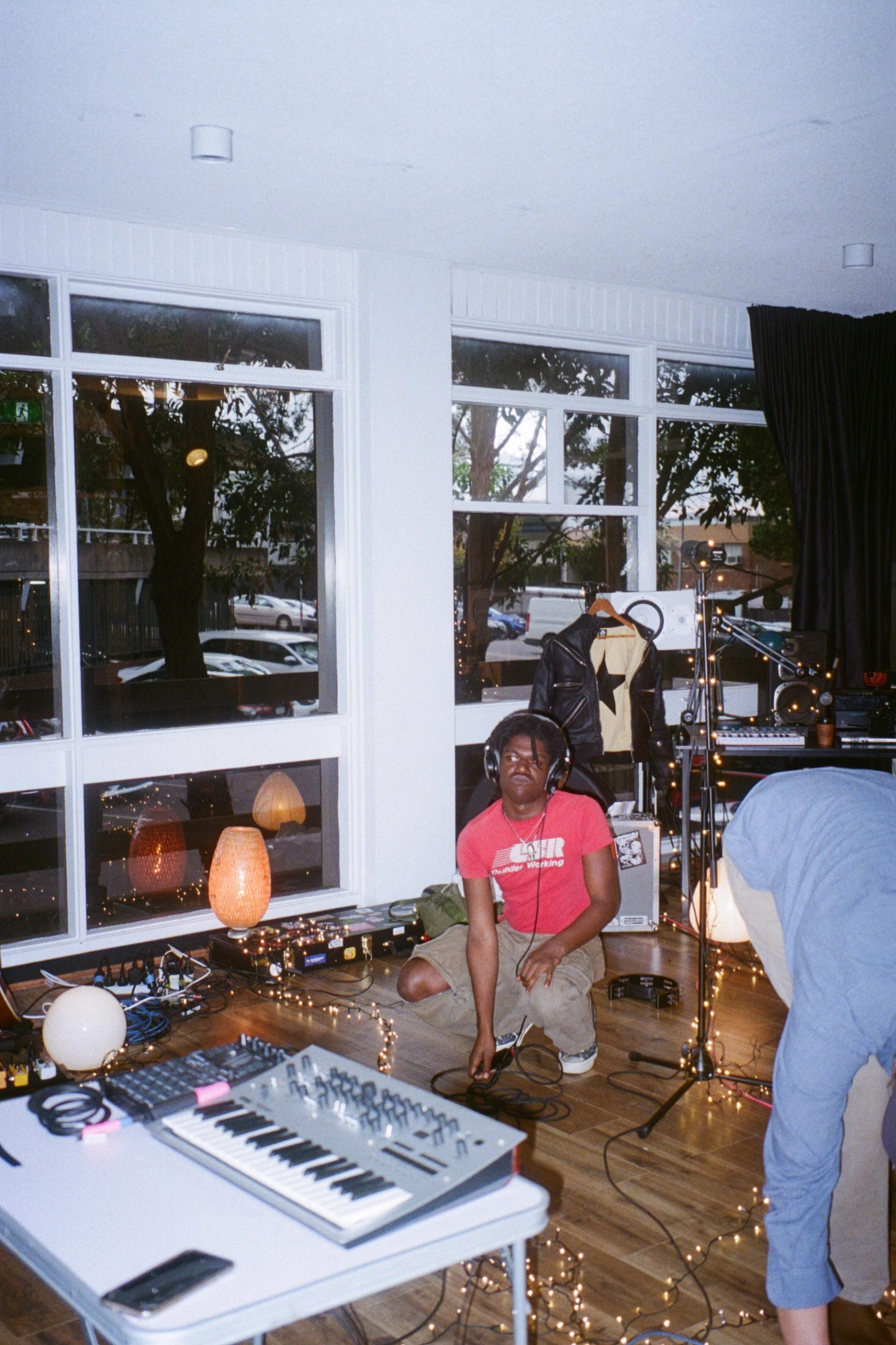 The musician Friday*, photographed in the studio he worked in during the Generations fellowship, crouched on the floor with headphones on