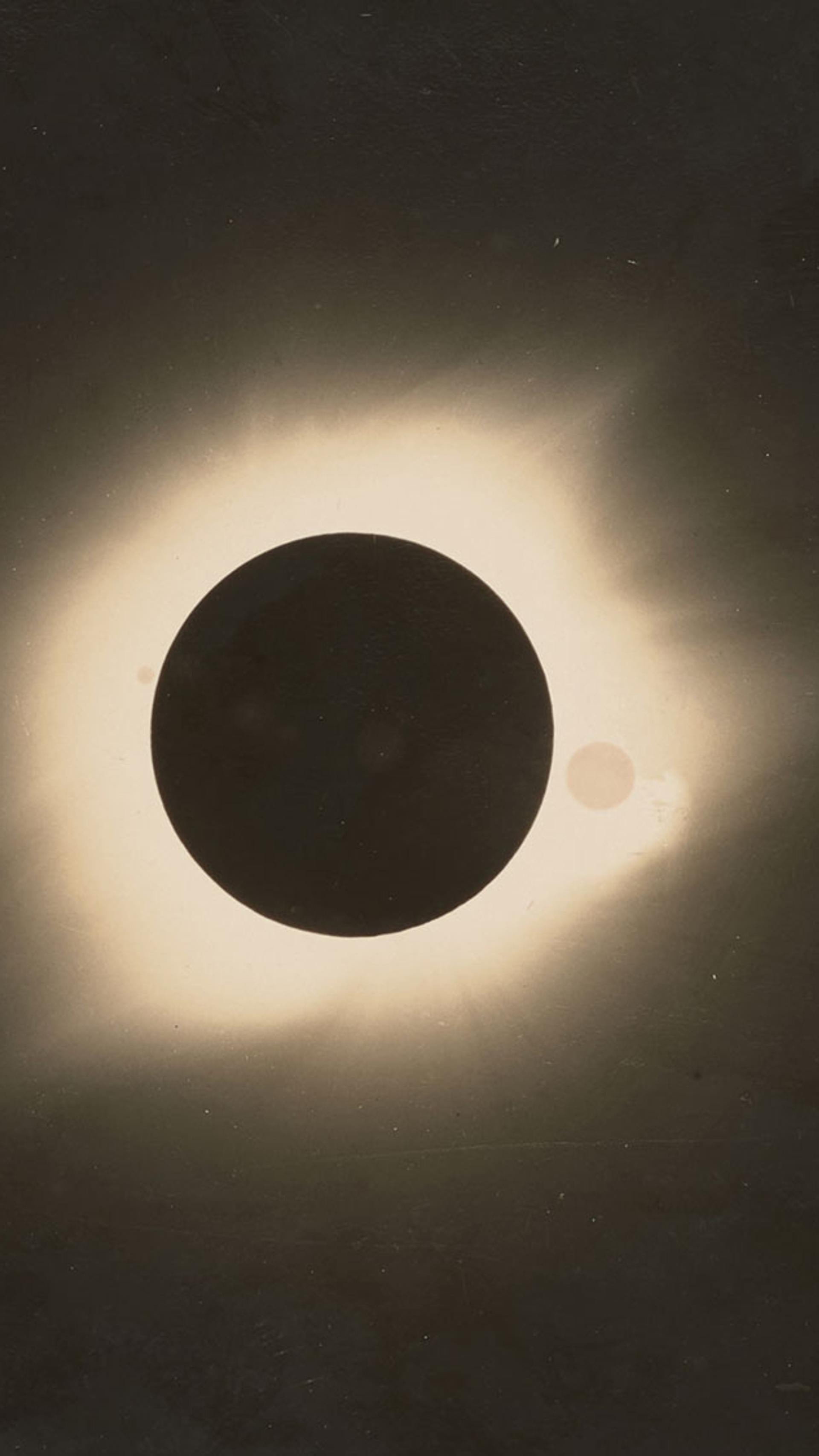 Black and white photograph of a total solar eclipse. Black circle in the centre with white glow around it, remainder of the image is black.