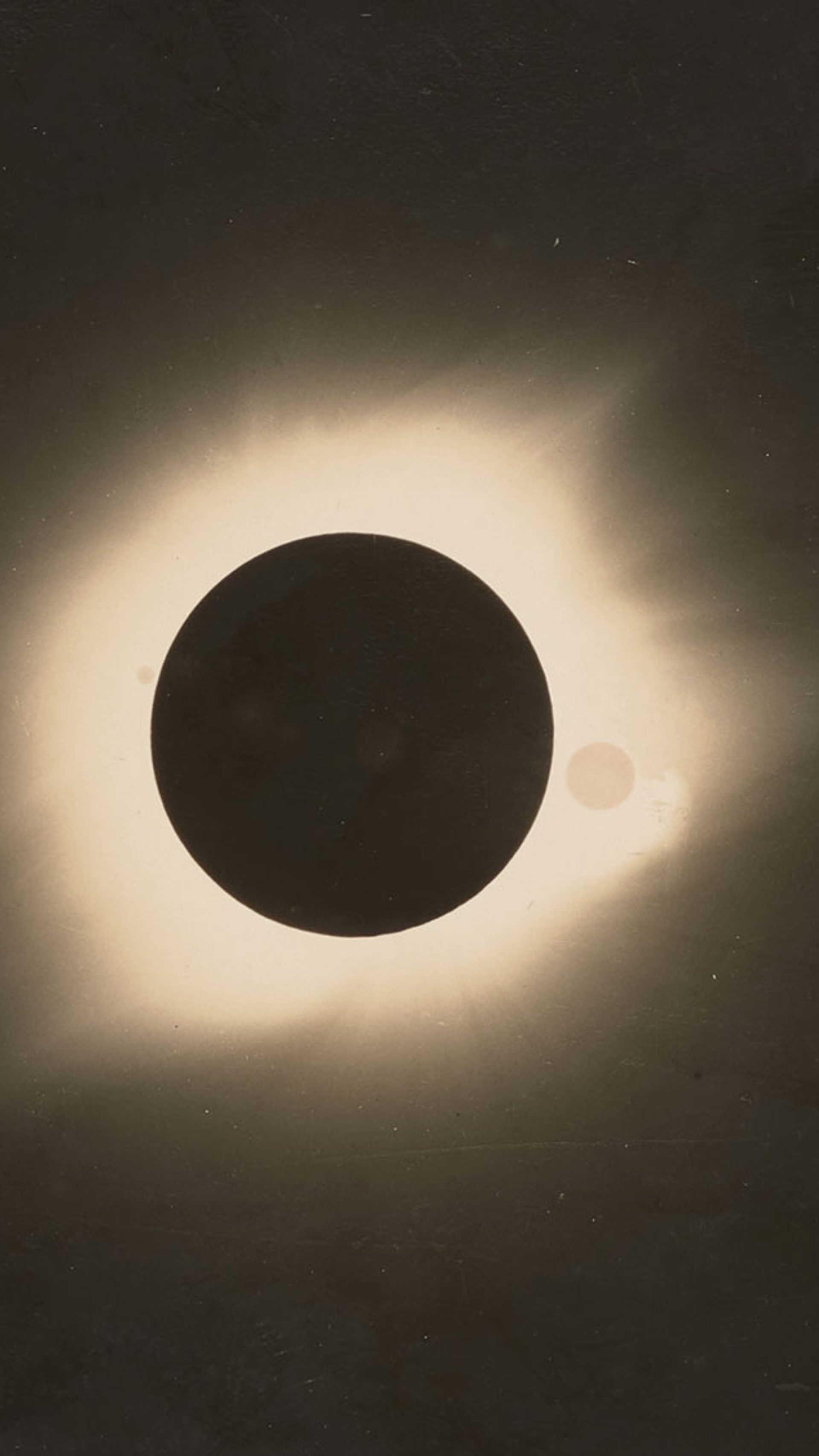 Black and white photograph of a total solar eclipse. Black circle in the centre with white glow around it, remainder of the image is black.