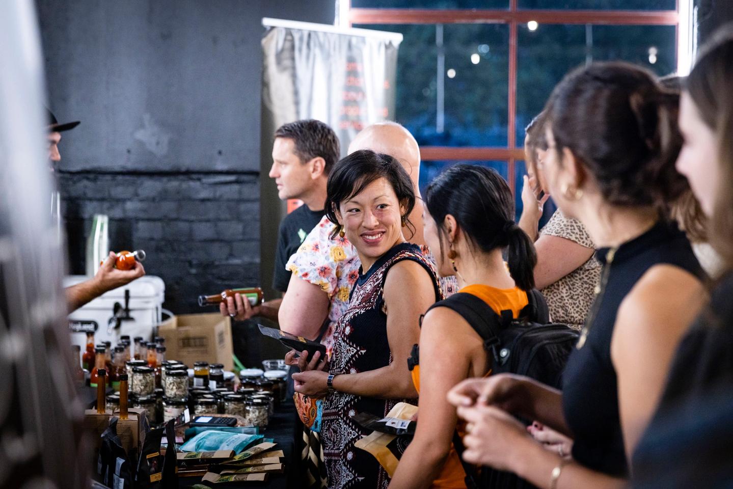 Smiling woman amidst a small crowd wanting to purchase Native Foodways products