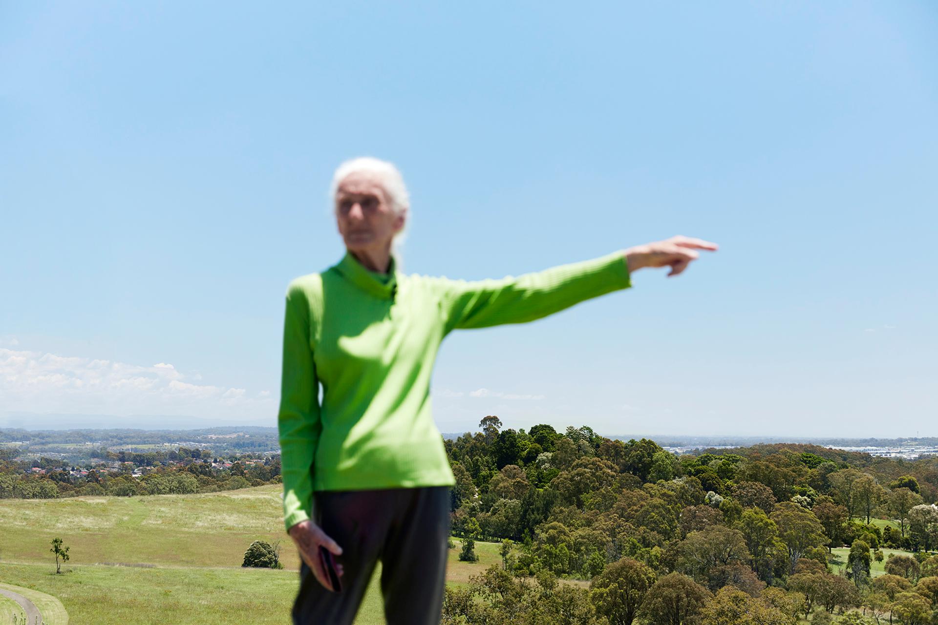 Elder woman pointed to the right, while standing out in the countryside.
