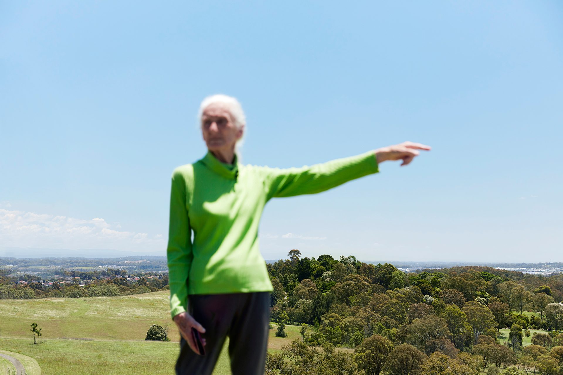 Elder woman pointed to the right, while standing out in the countryside.