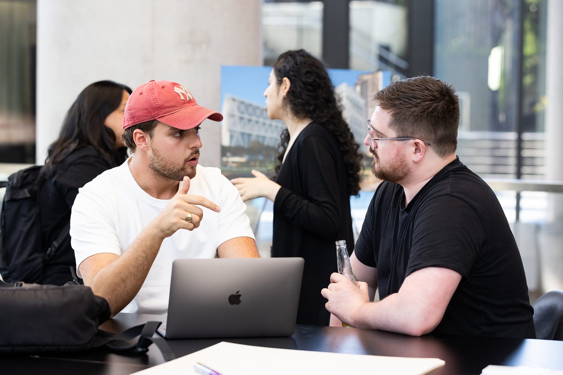 Two humans discussing ideas over a laptop, with two more in the background.