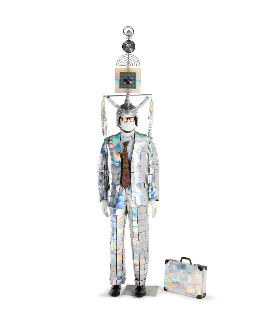 Two piece wool flannel suit, shirt and accessories with applique holograms and found objects (recycled suit, new accessories). Accessories include headpiece comprising motorcycle helmet, perspex, hologram foils, compact discs and plastic squids; 'scorpion skin' plastic tie; pair of purple nylon socks; pair of hologram eyes glasses; briefcase of clear plastic with applied holograms.