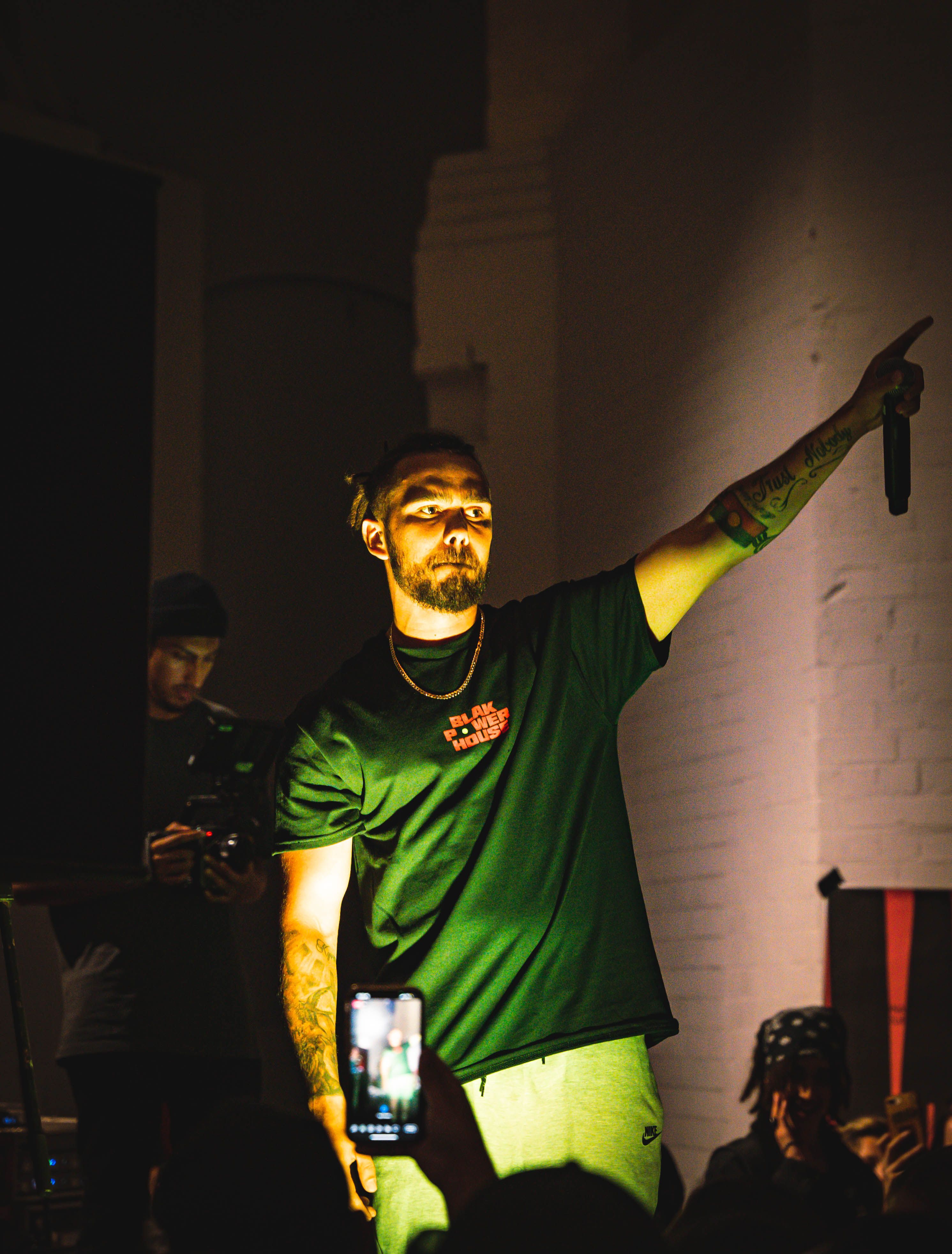 A young man is standing on stage mid performance and holding a microphone in his left hand.