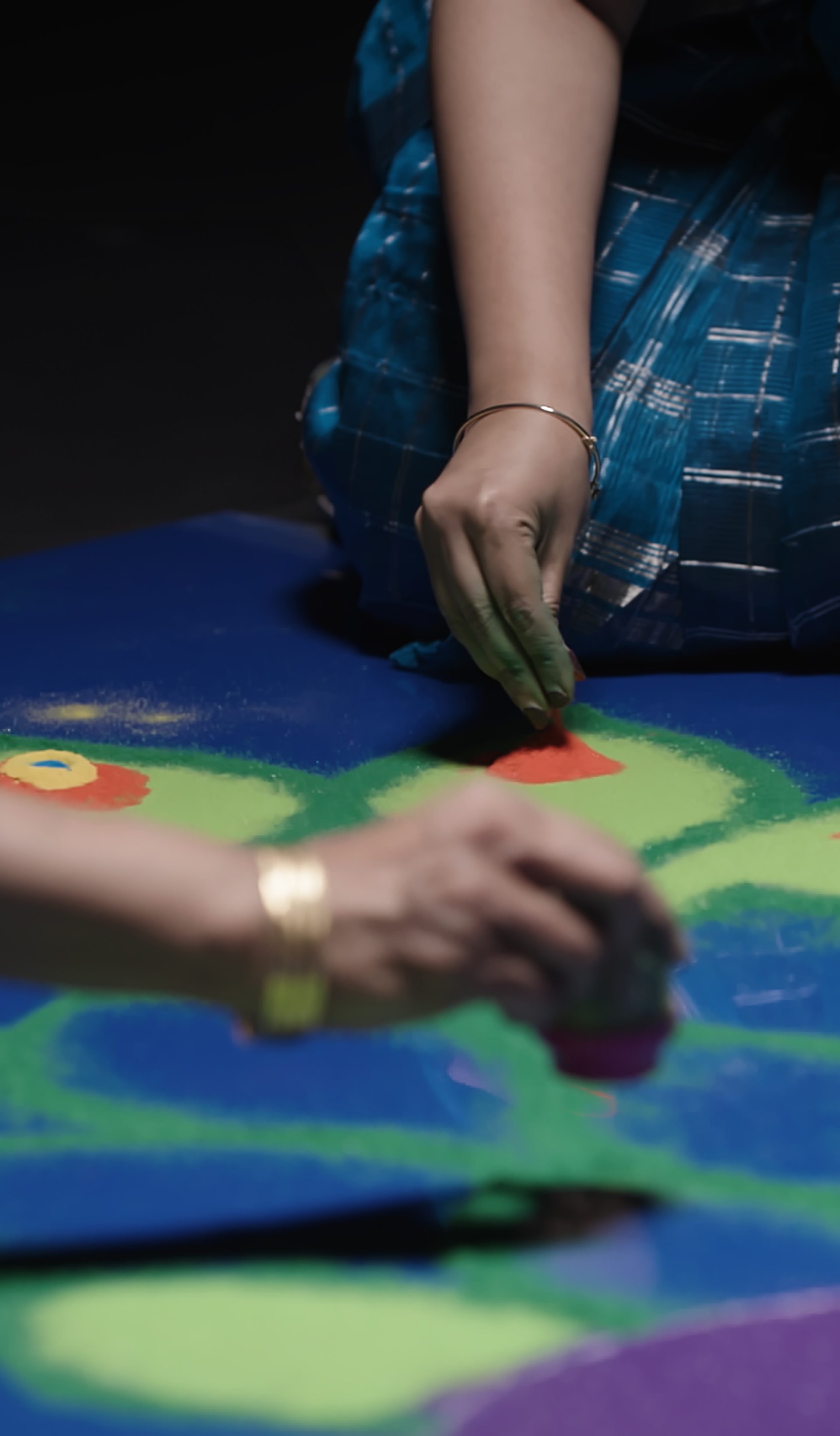 Two women create Rangoli artwork.