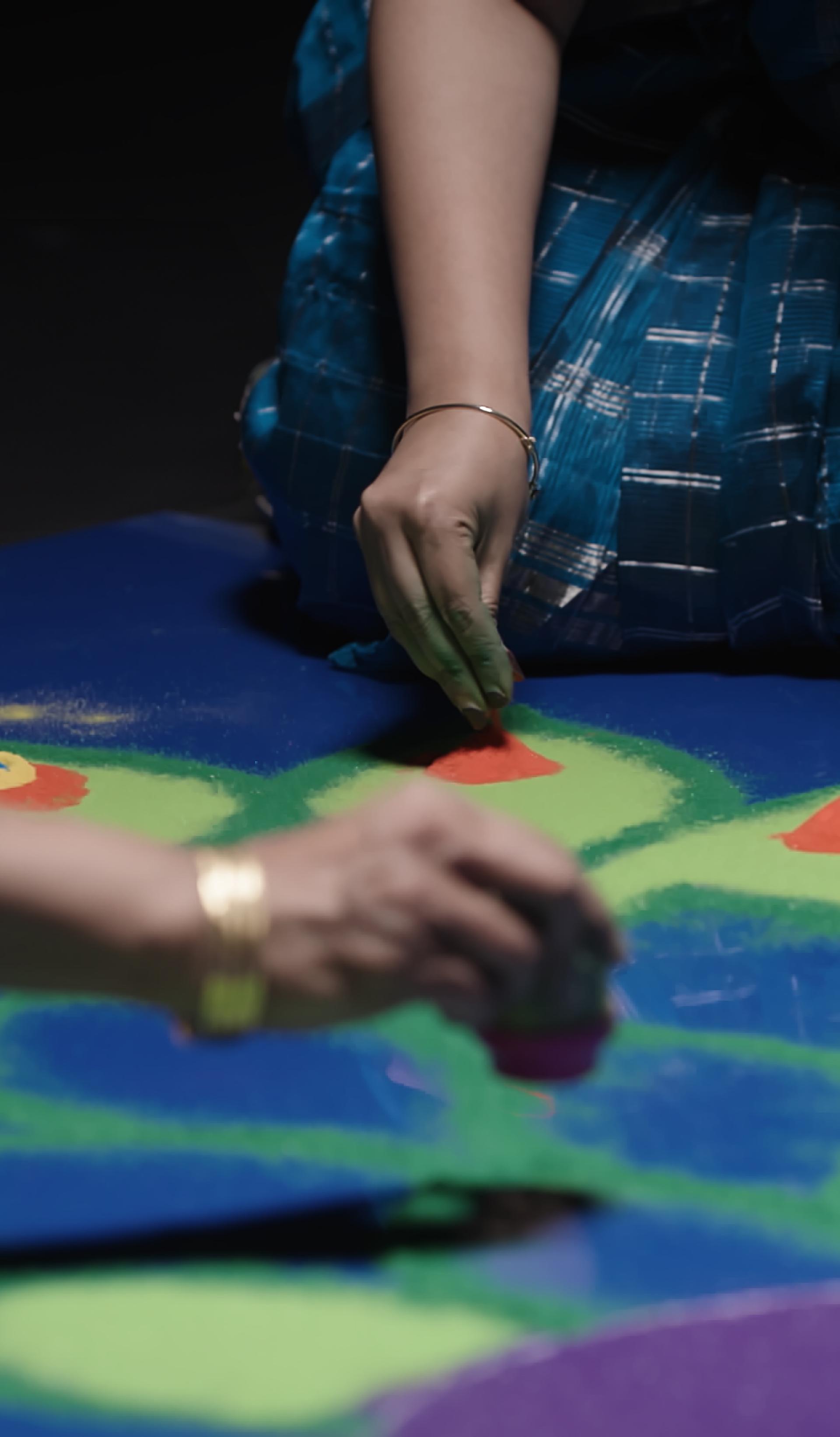 Two women create Rangoli artwork.