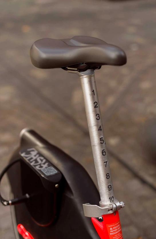 A brown electric bike seat with numbers 1-10 written on the pole connecting the seat to the bike.