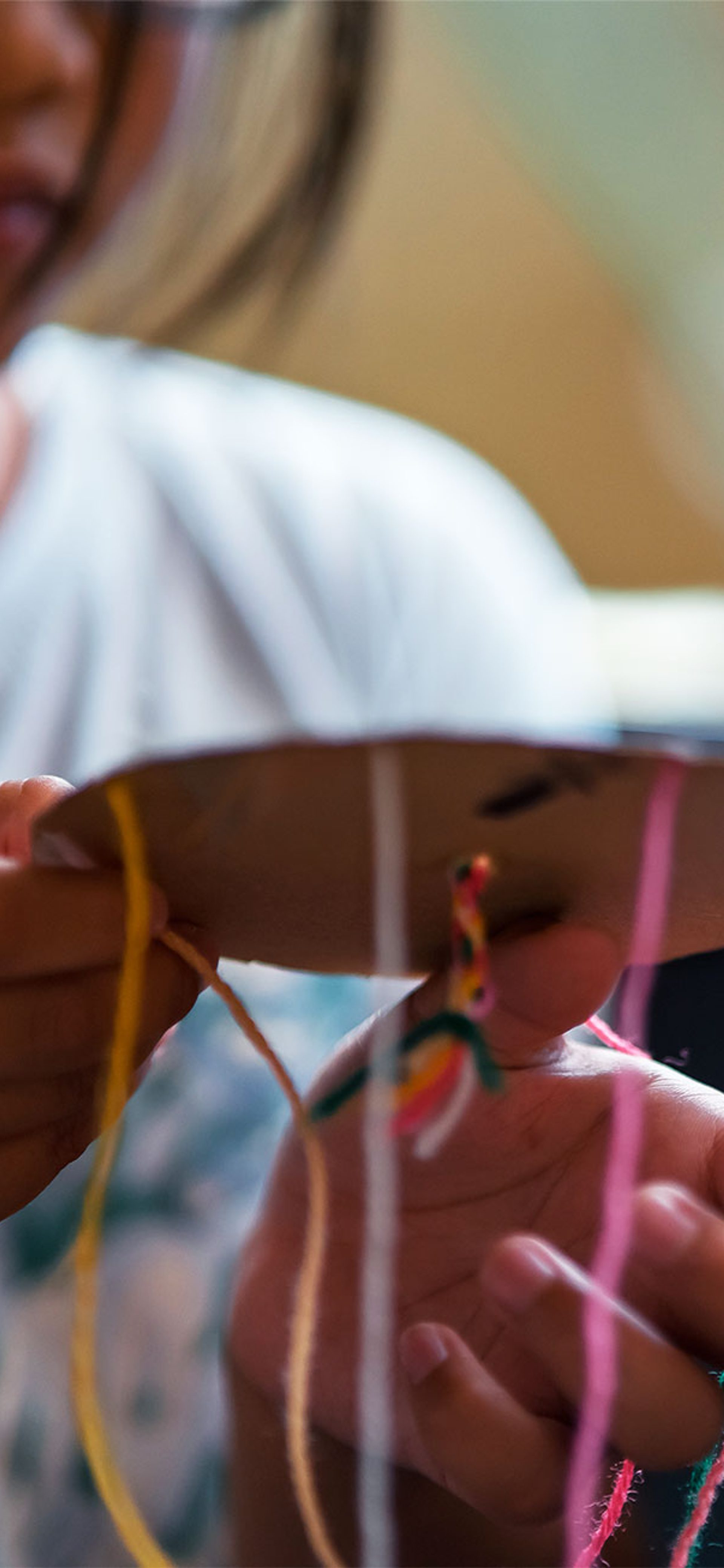 A child with a long braid creates an artwork using cardboard and coloured yarn.