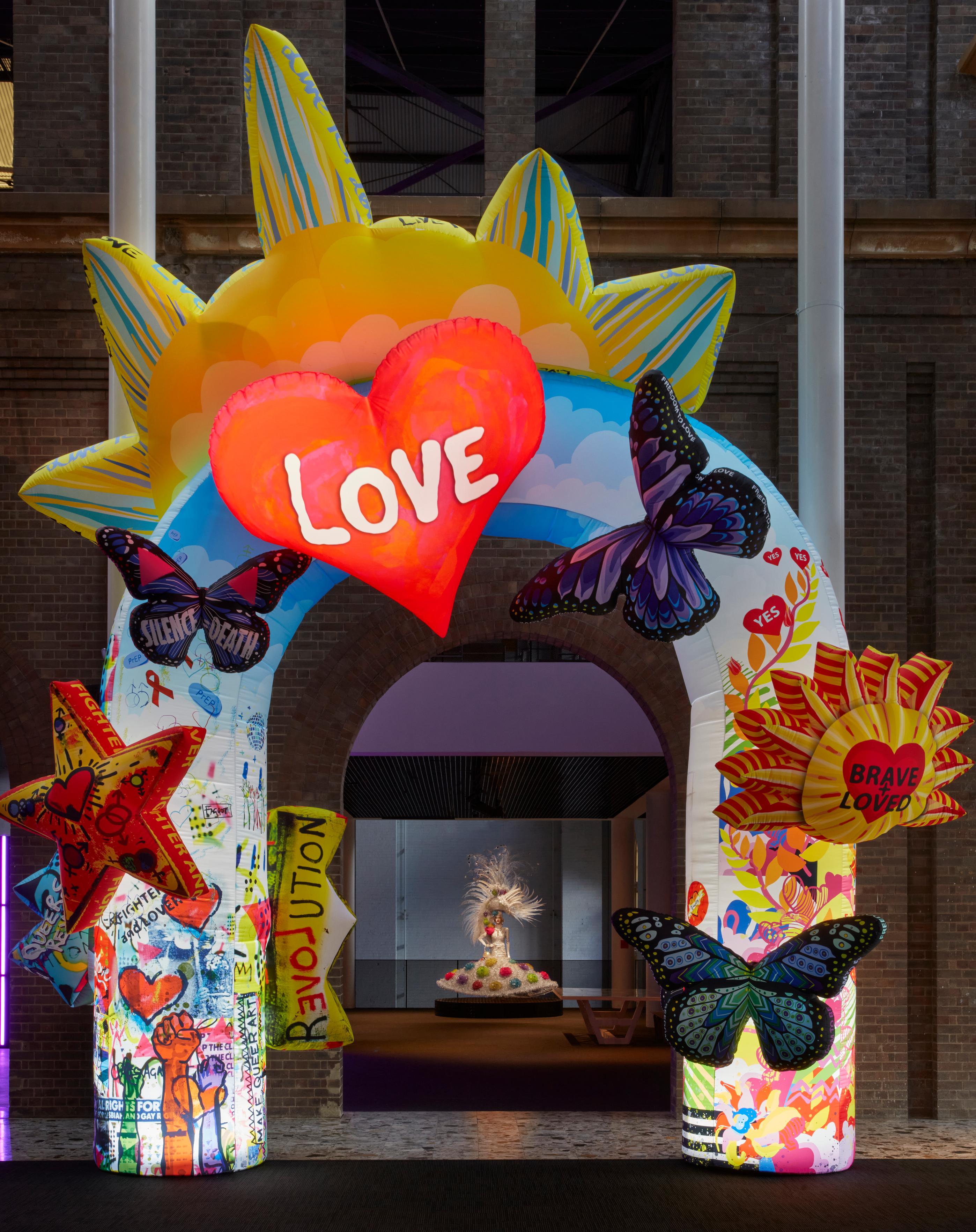 A blow up archway with an additional blow up sun rising behind it. Attached to the arch are blow up butterflies, stars, the sun, and a love heart with ‘LOVE’ written inside.