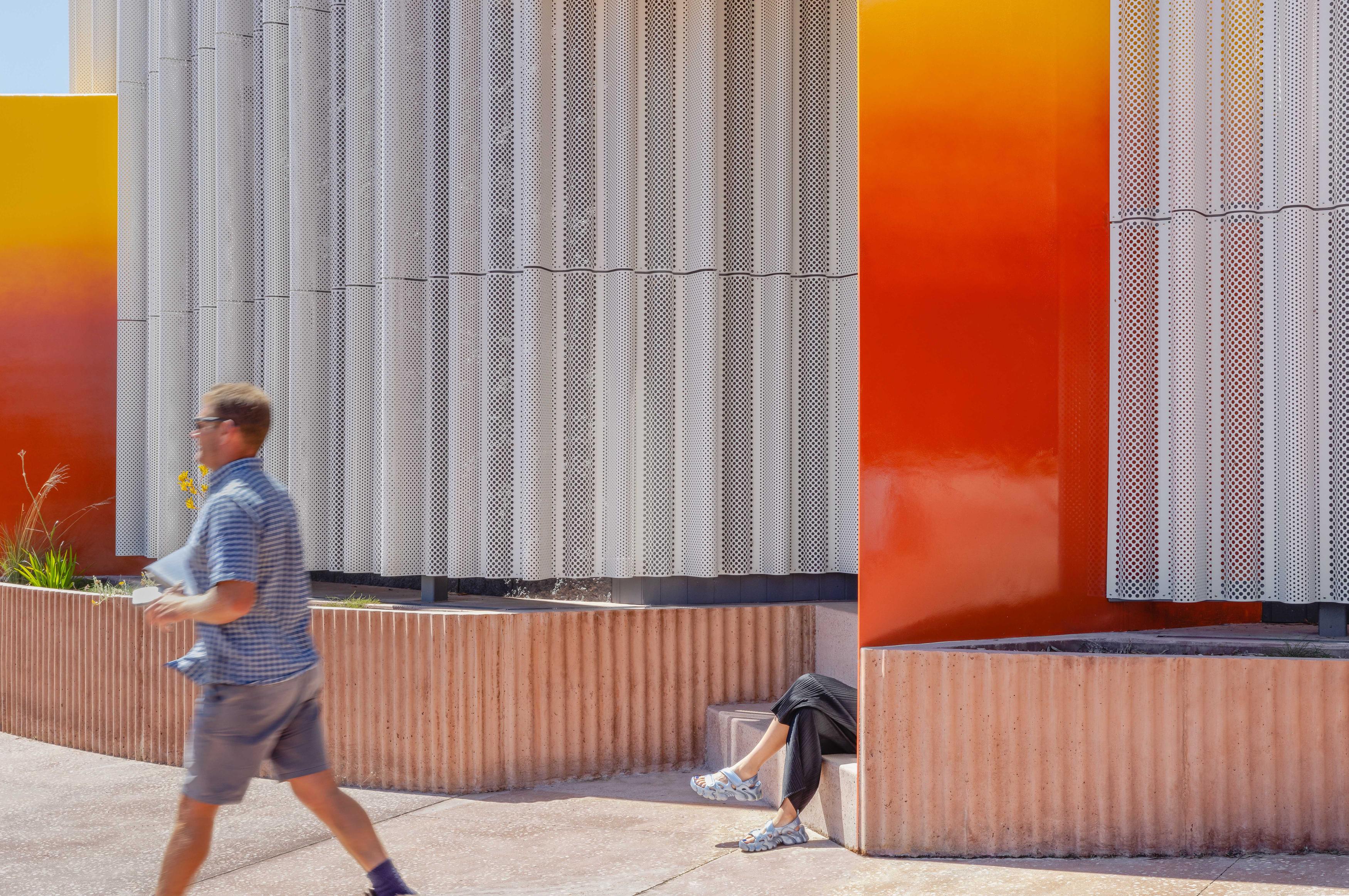 Person walking past colourful and metallic wall scape.